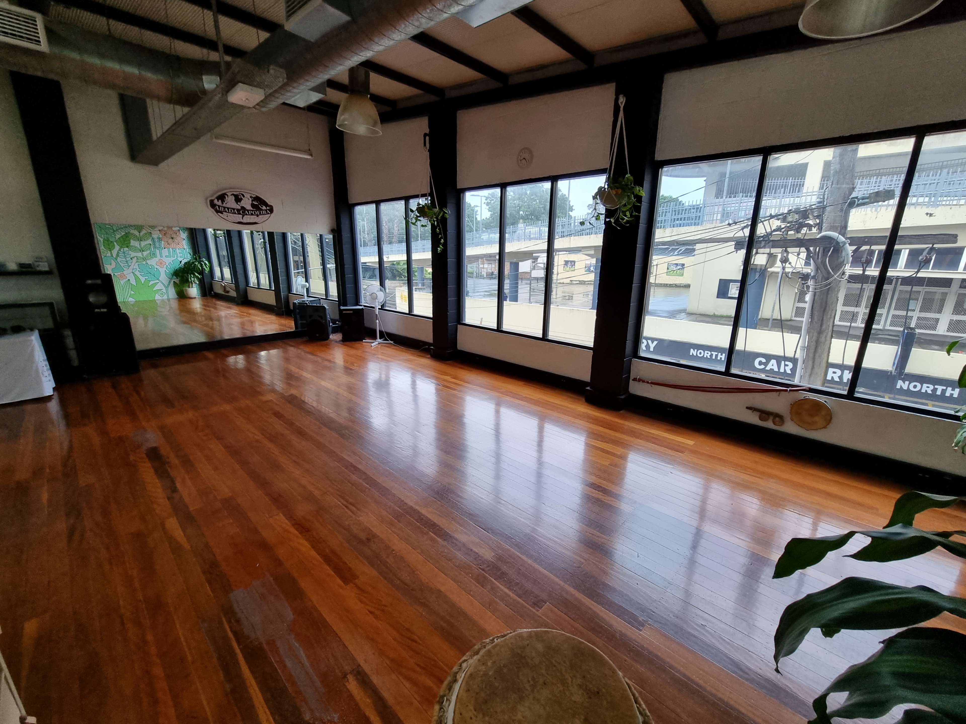 A spacious fitness studio with wooden floors and large windows, providing a view of the outside.