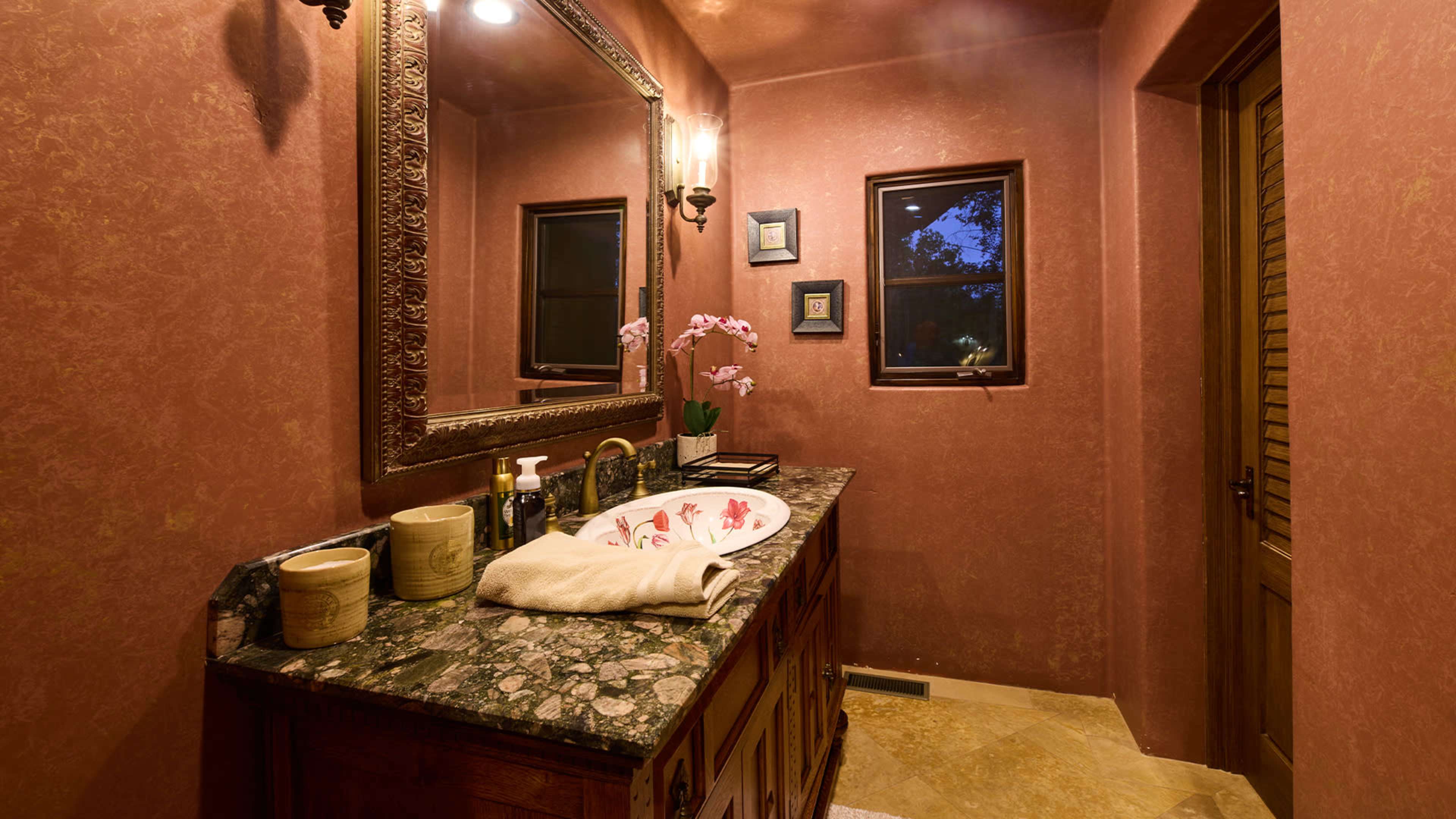 A bathroom featuring a marble countertop with a sink, an ornate mirror, and decorative elements like orchids and framed pictures on the walls.