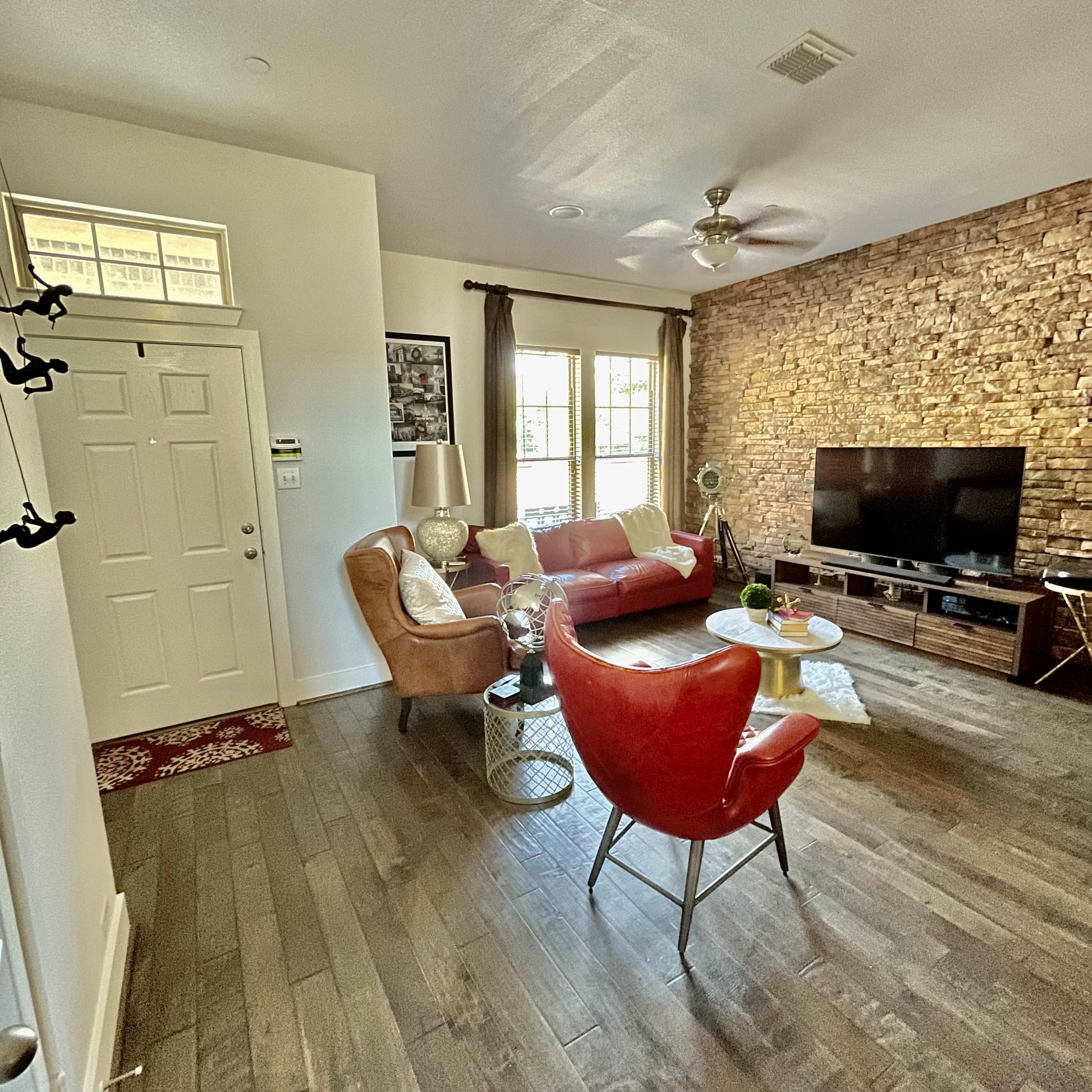 The living room features a stone accent wall, a red armchair, a brown couch, and a television stand with a large TV.
