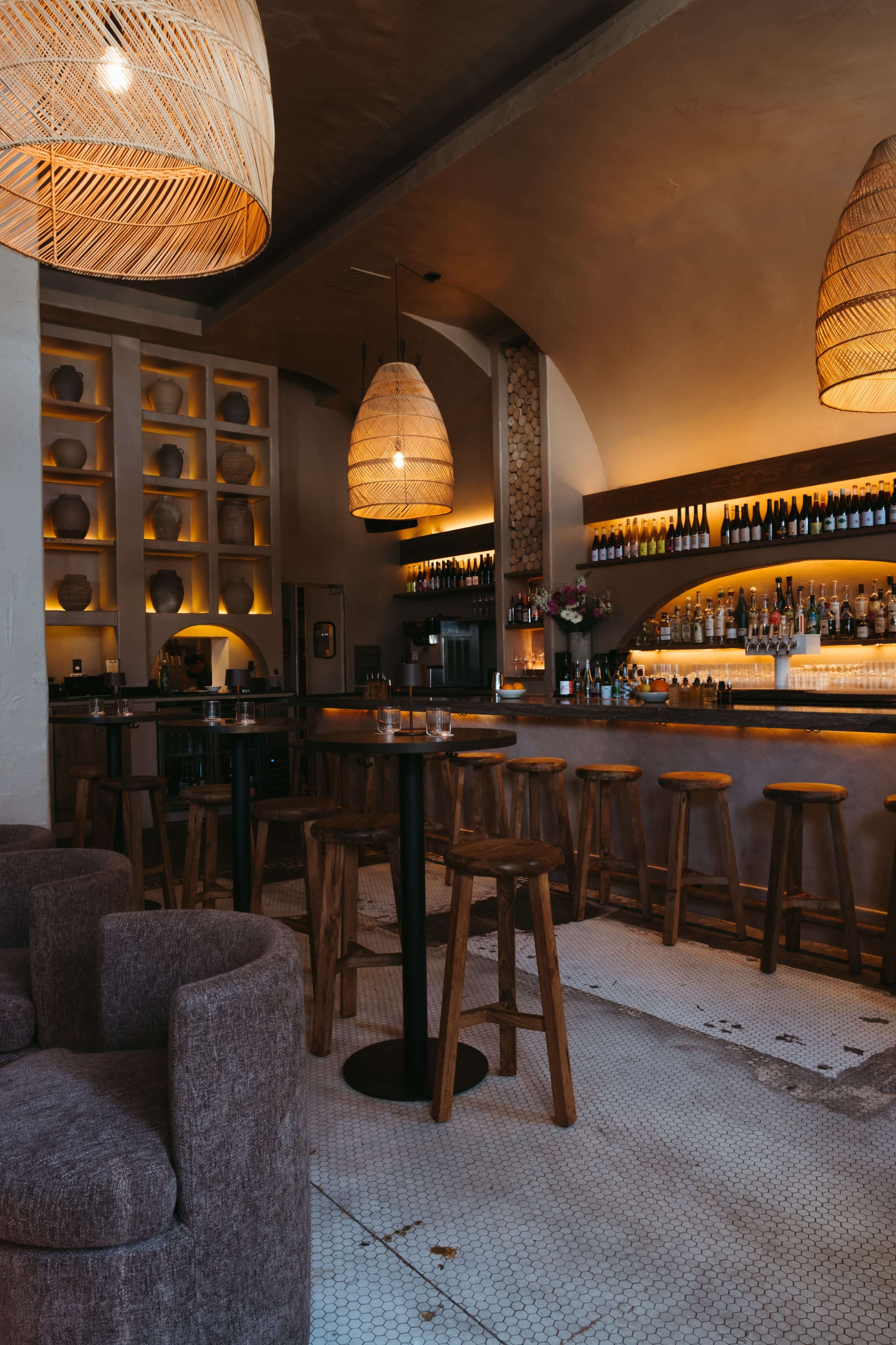 A well-lit bar area features wooden stools, a curved counter, and decorative light fixtures overhead.