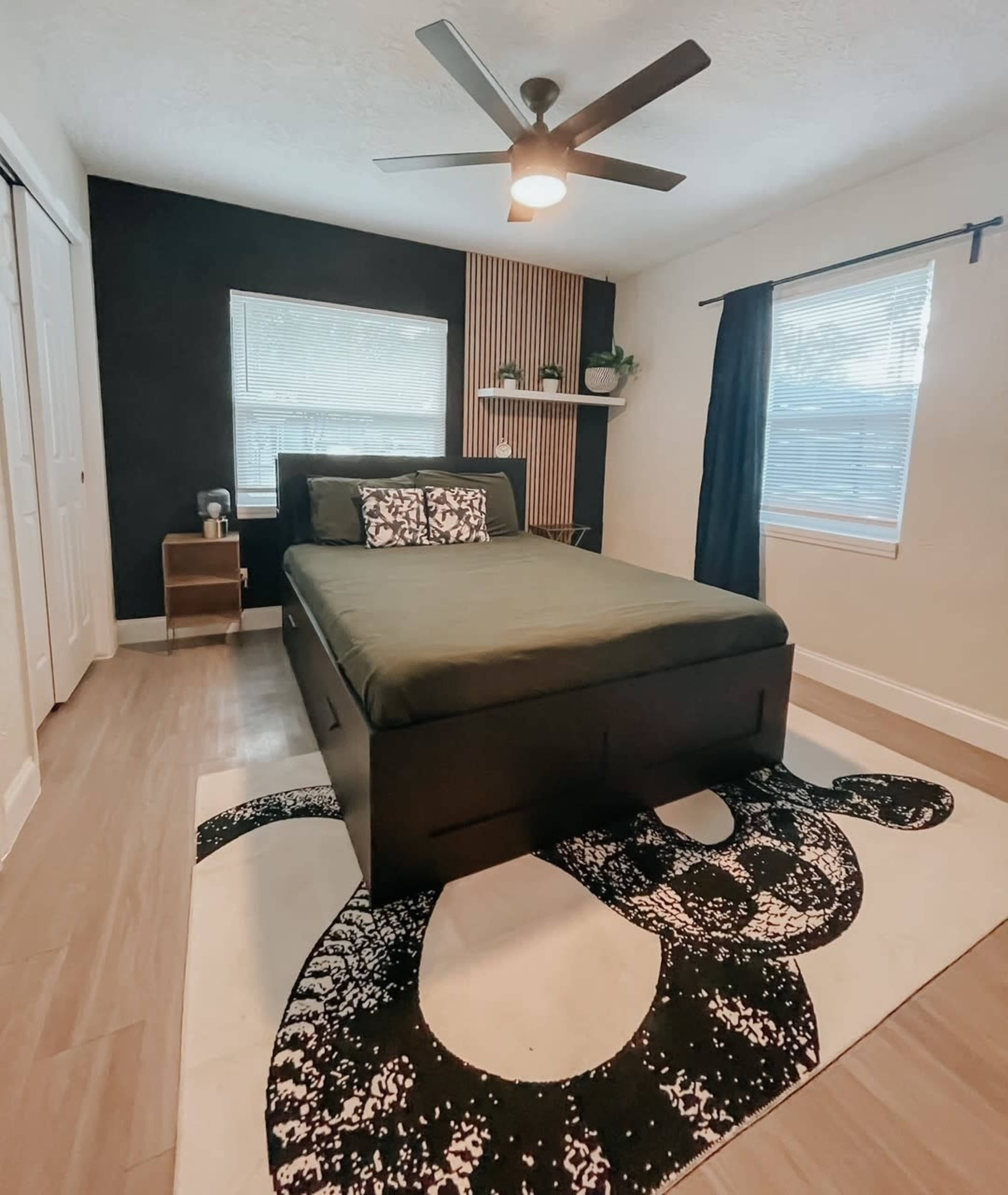 A modern bedroom features a black and green color scheme with a bed, nightstand, and a large rug displaying a snake design.