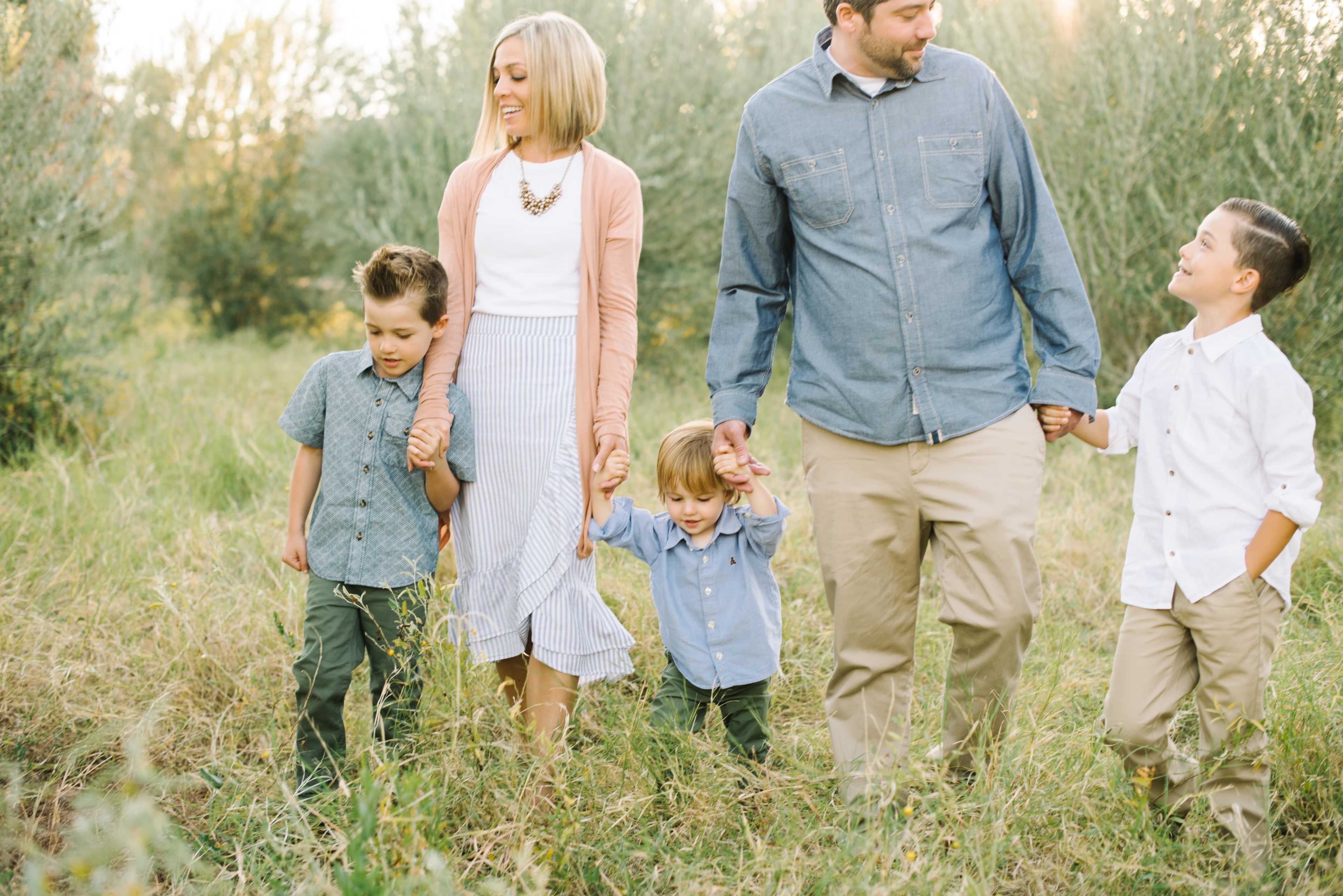 A family of five walks hand-in-hand through a grassy area with trees in the background.