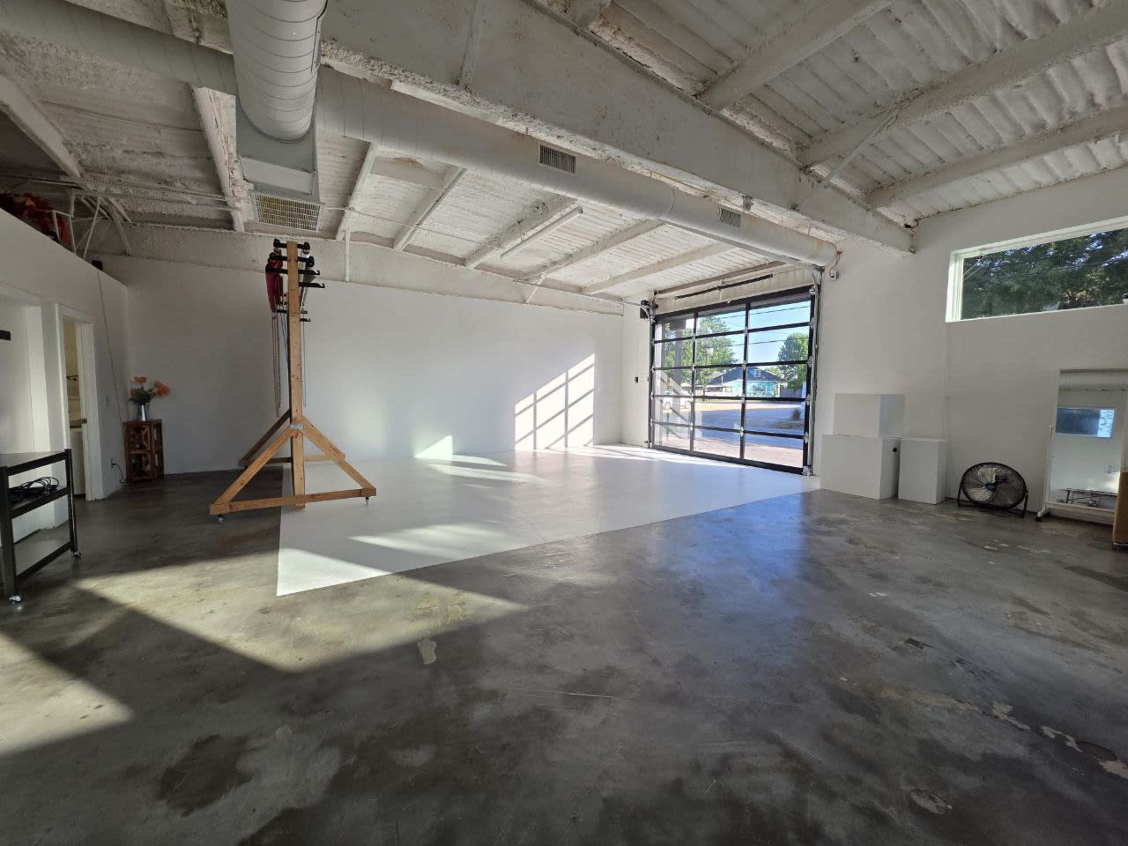 The image shows an empty studio space with a polished concrete floor, large windows, and a minimalist design featuring a white backdrop and studio equipment.