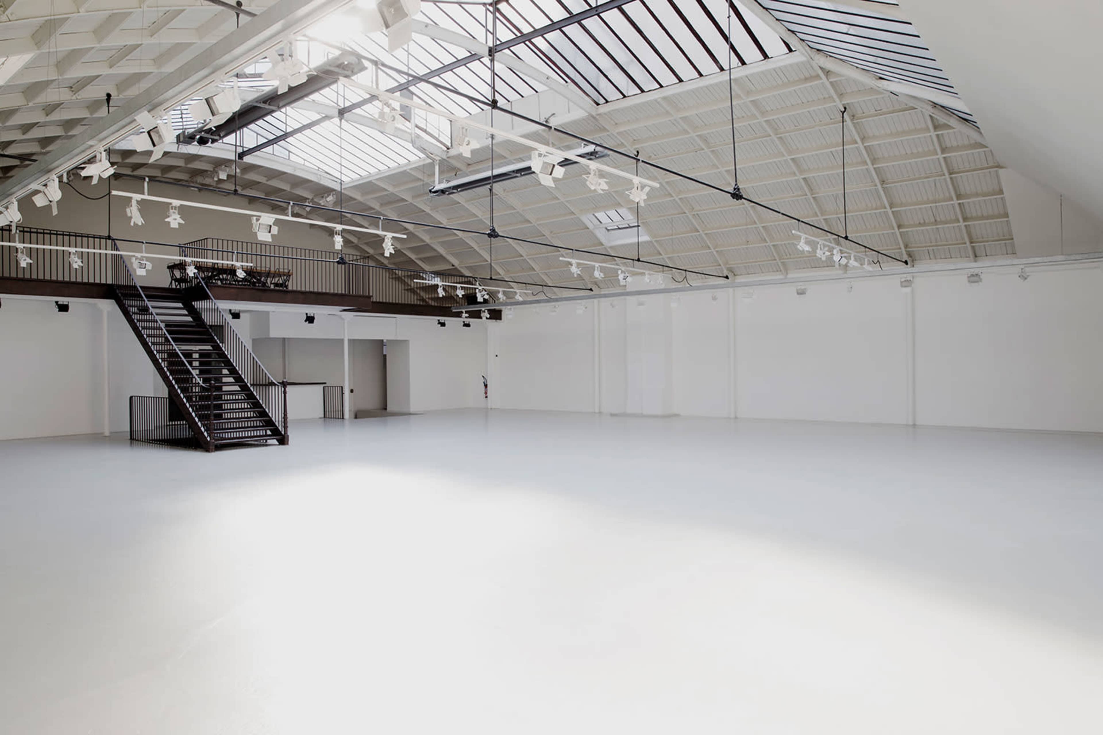 A spacious, empty room with a high ceiling, large skylights, and a staircase on one side.