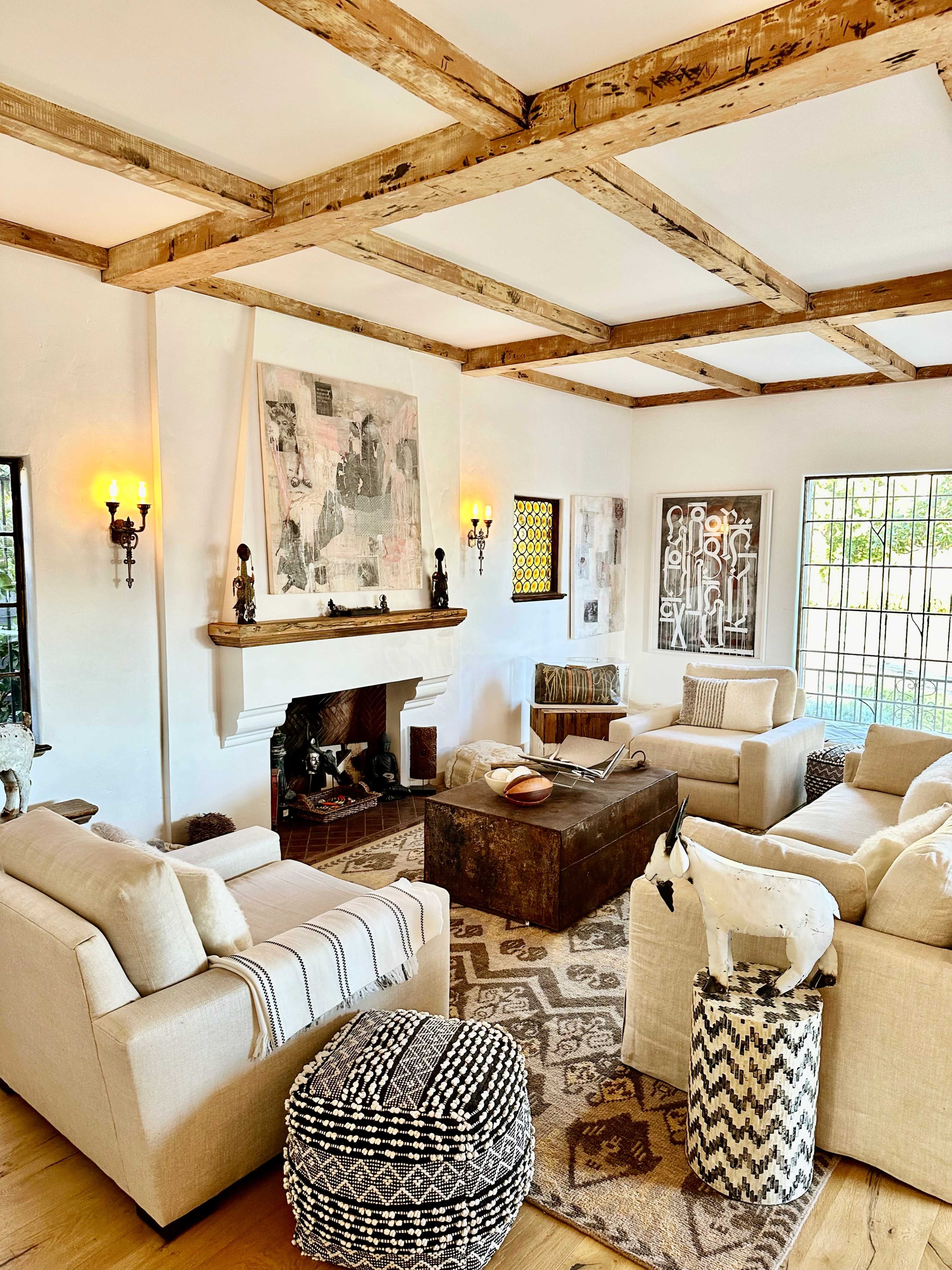 The living room features a cozy arrangement of beige sofas around a wooden coffee table, with a fireplace, art on the walls, and decorative accents throughout.