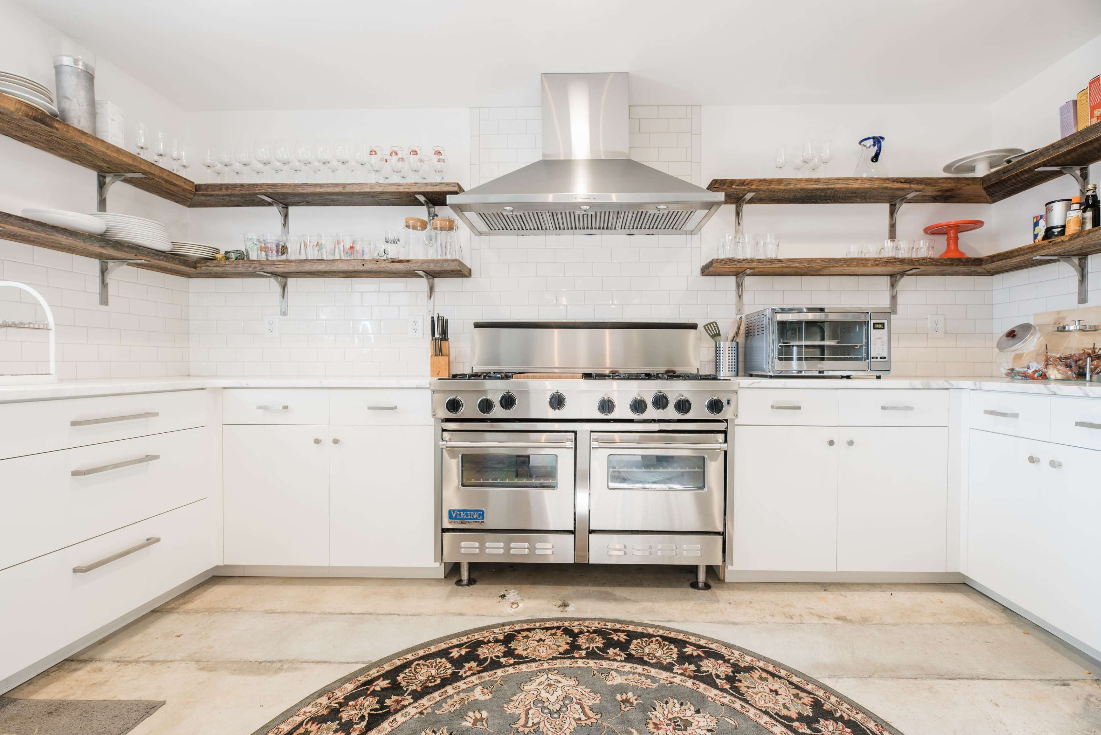 A modern kitchen with stainless steel appliances, white cabinetry, and wooden open shelving displaying glassware.
