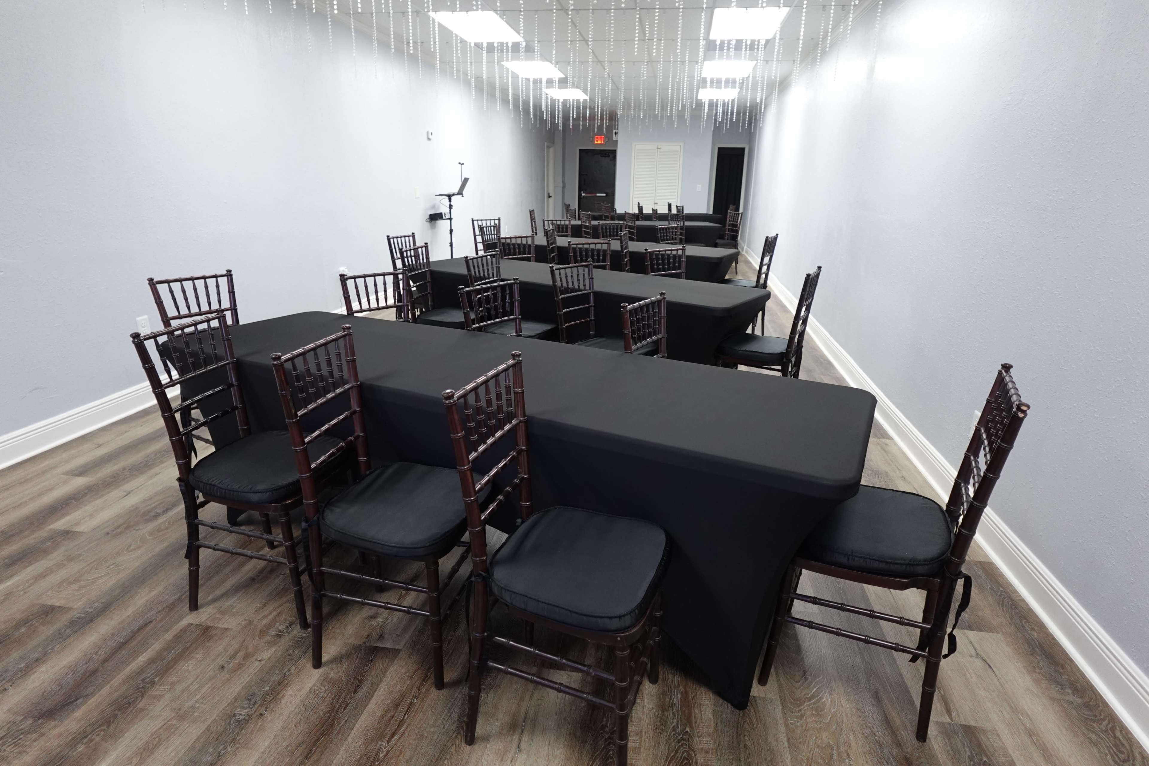 A spacious room arranged with multiple tables covered in black cloth and surrounded by black chairs.