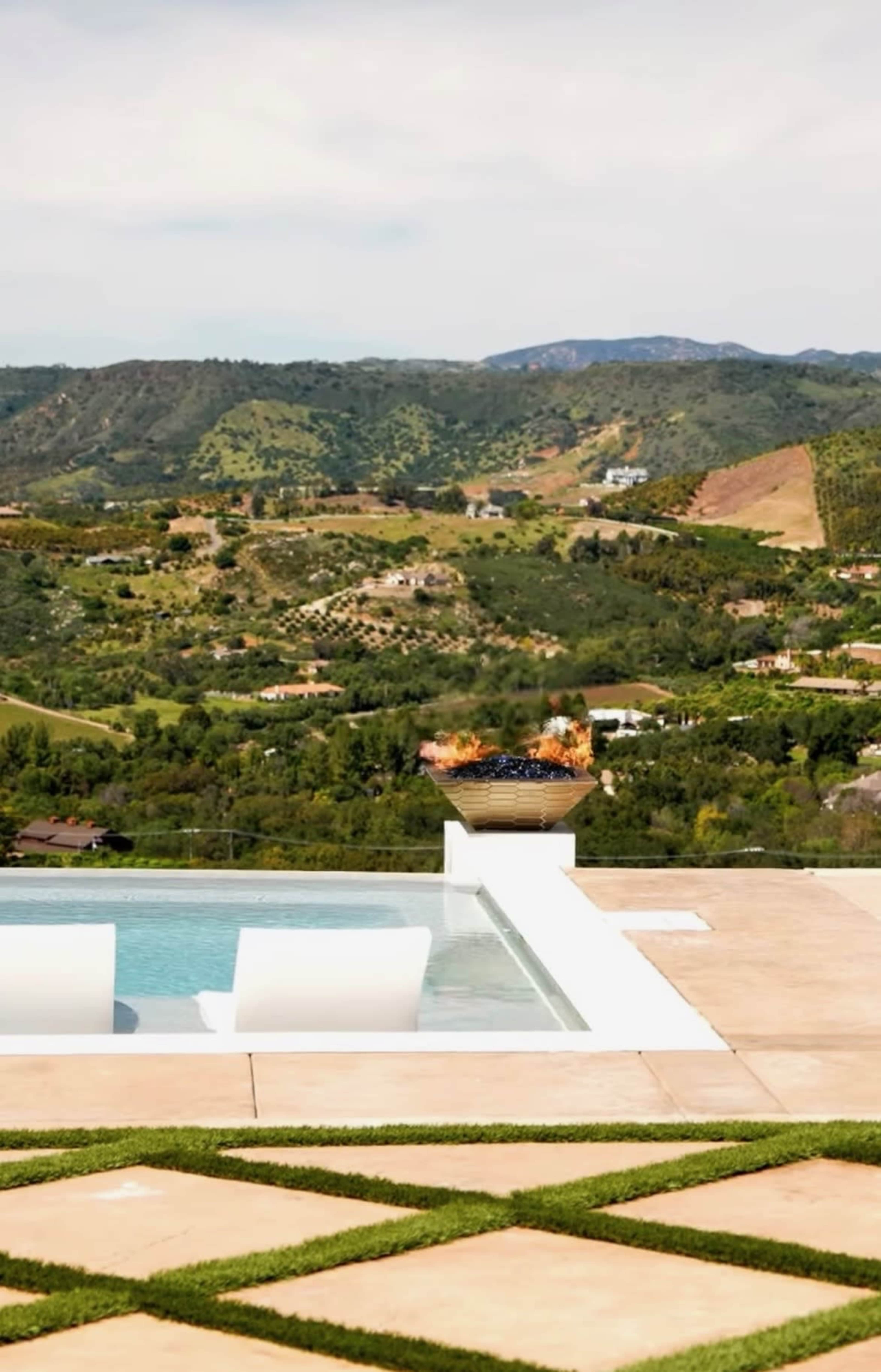 A swimming pool with white lounge chairs overlooks a lush hillside landscape in the background.