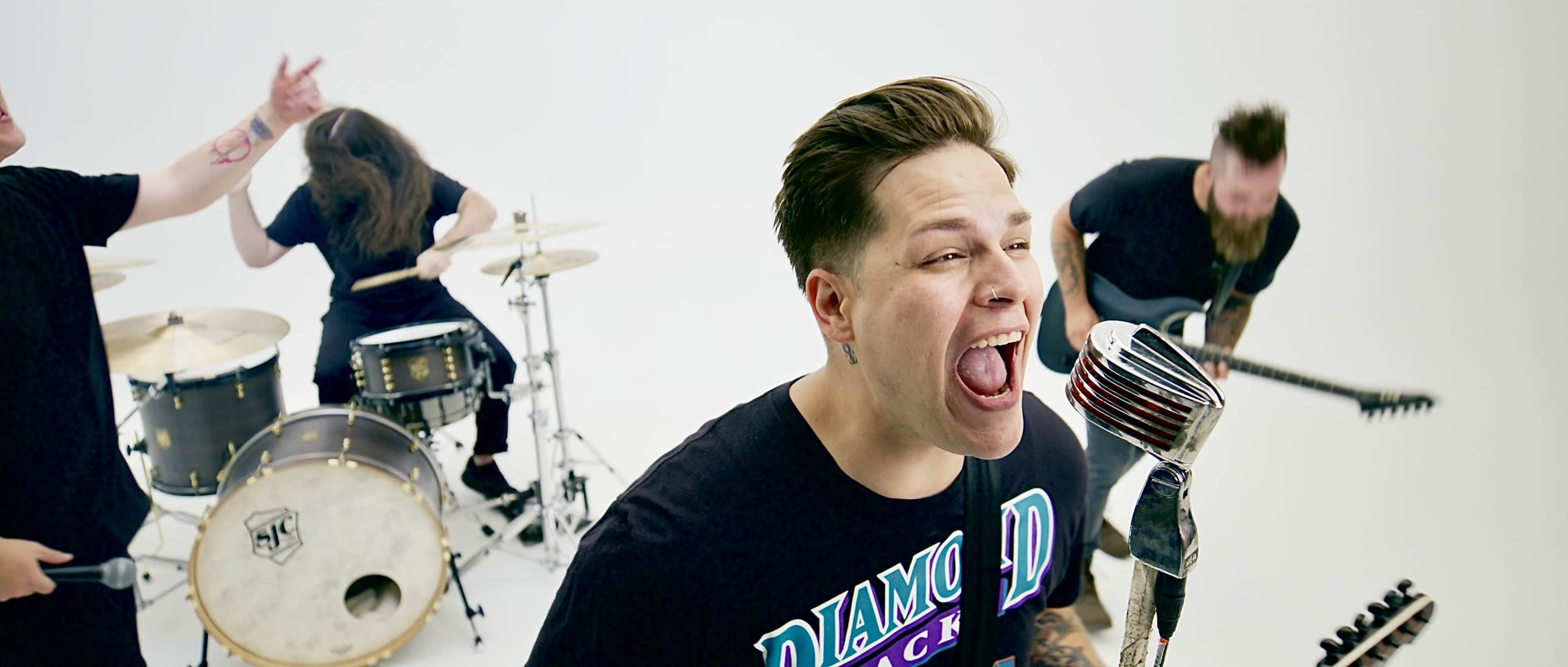 A rock band performs energetically in a brightly lit studio with a white backdrop.