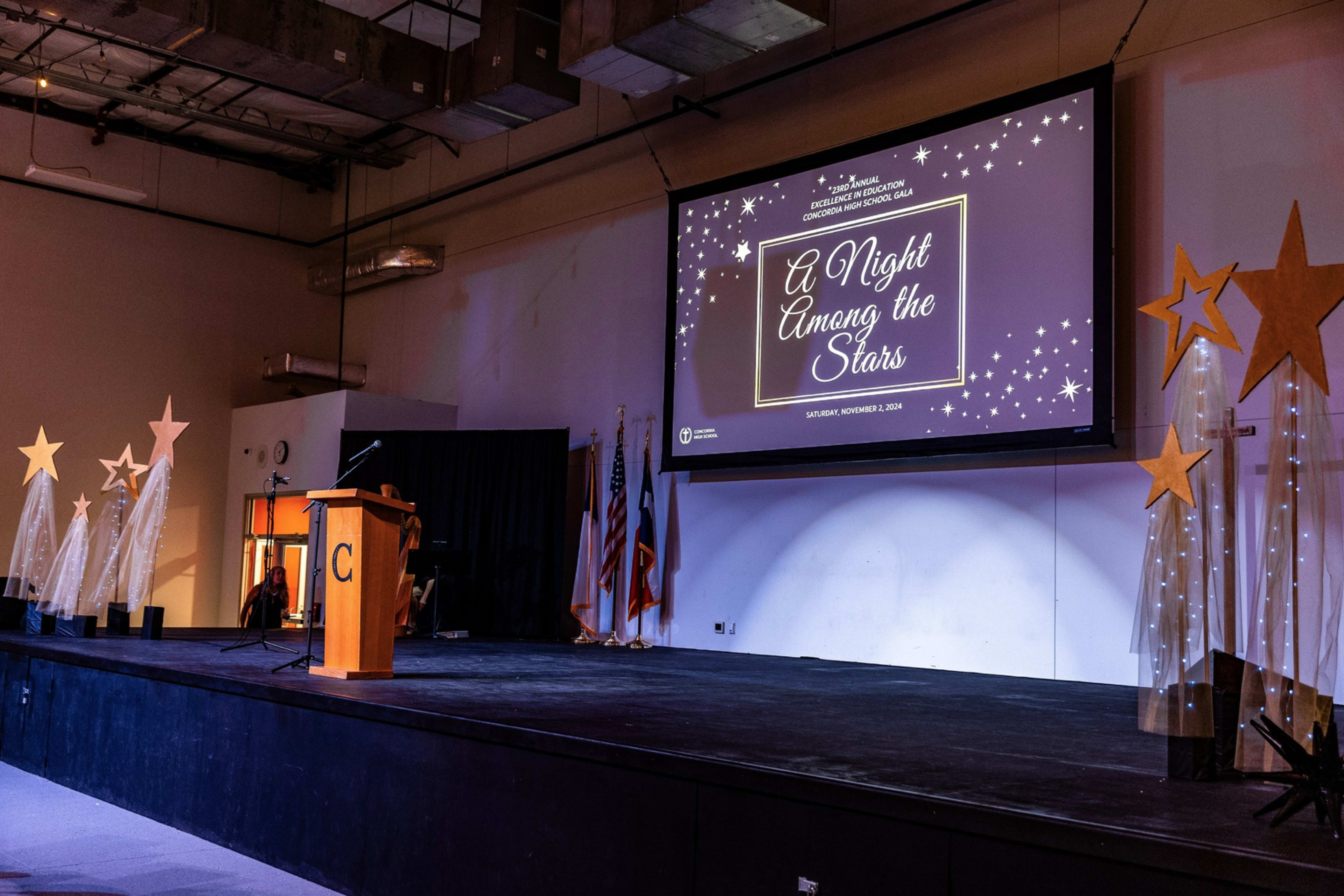 The image shows a stage set up for an event titled "A Night Among the Stars," featuring a podium, a large screen displaying the event title, and decorative star-shaped elements on either side.
