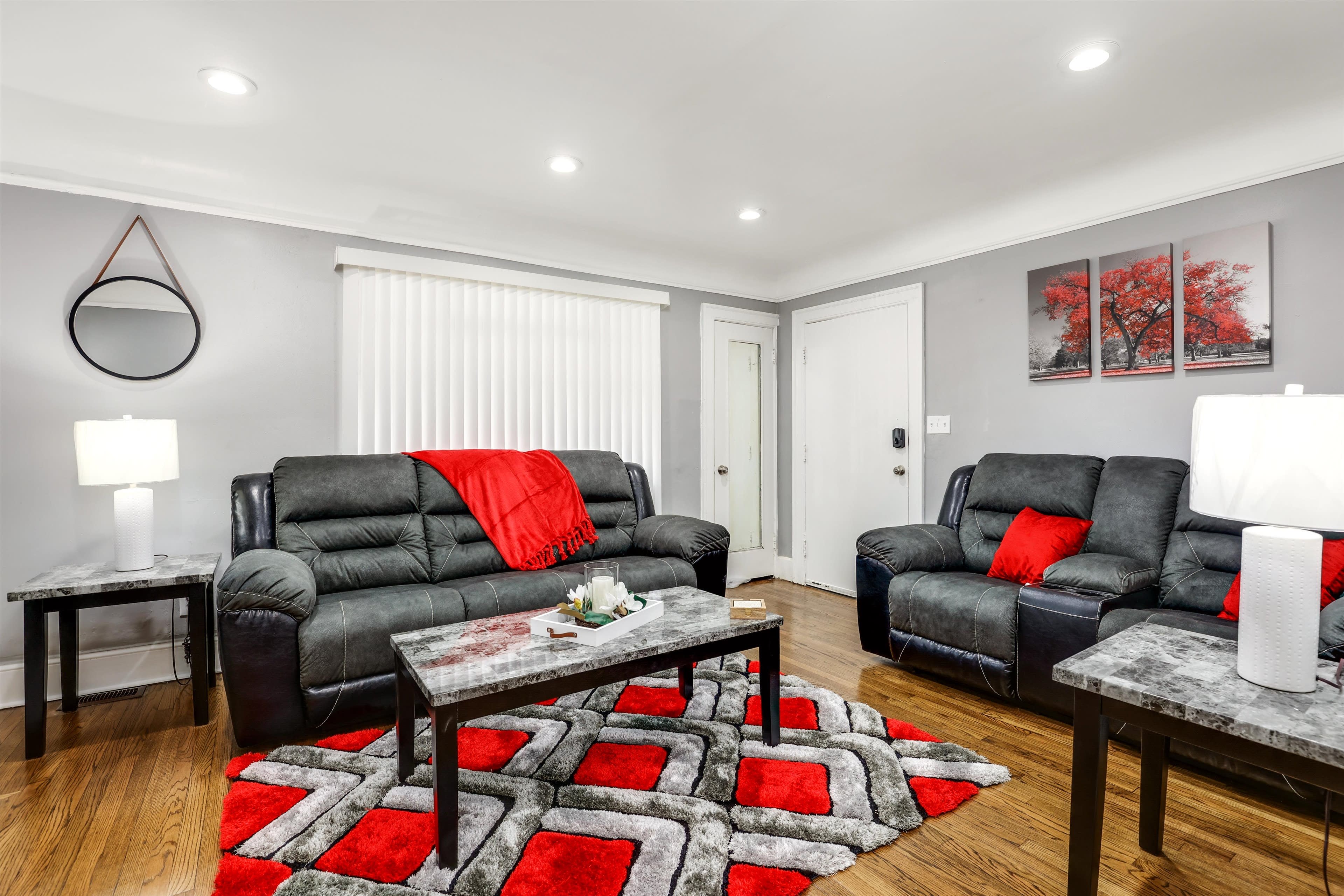 The living room features dark sofas with red accents, a patterned rug, and modern lighting, complemented by artwork on the walls.