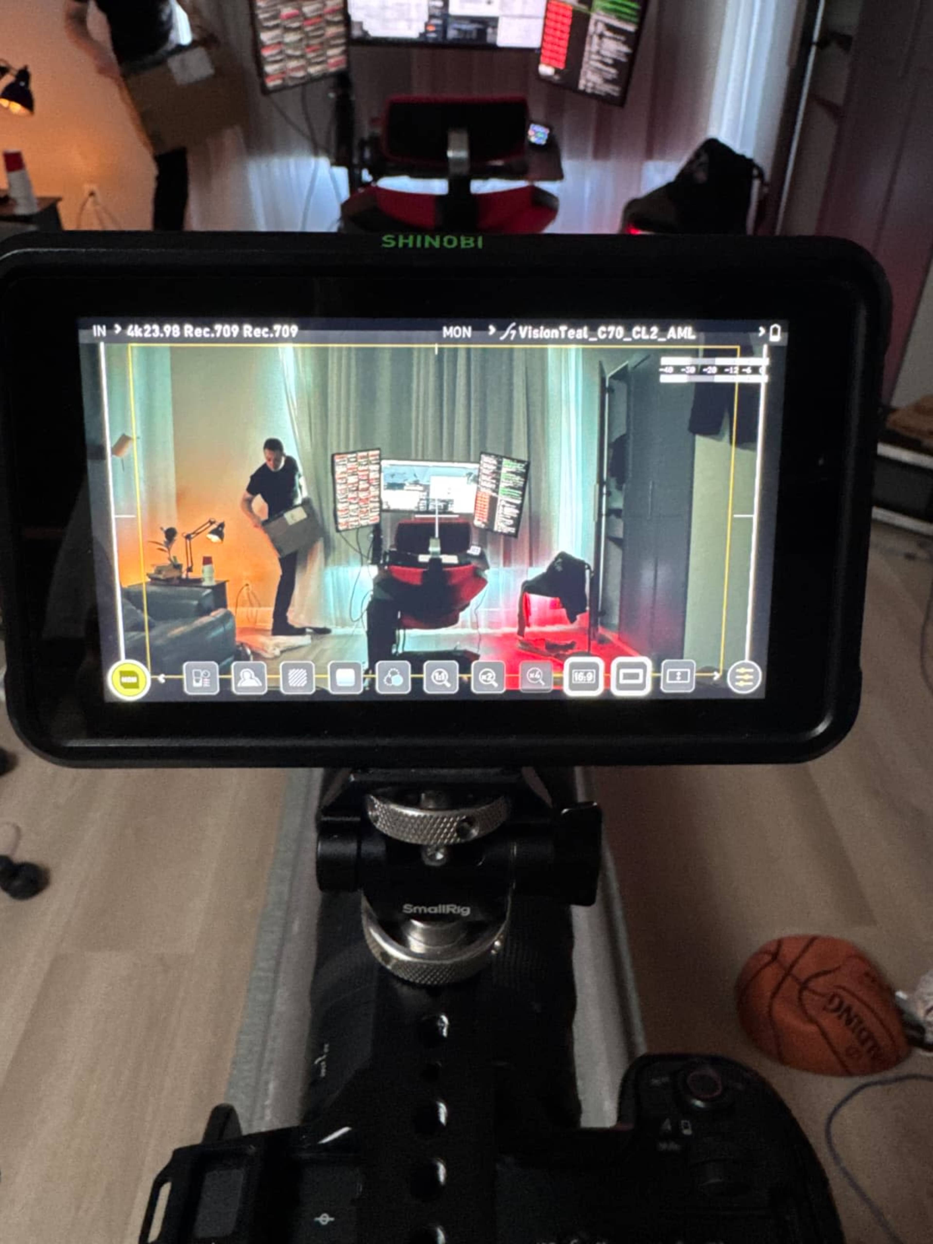 A camera monitor displays a scene featuring a person in front of multiple screens in a well-lit studio environment.
