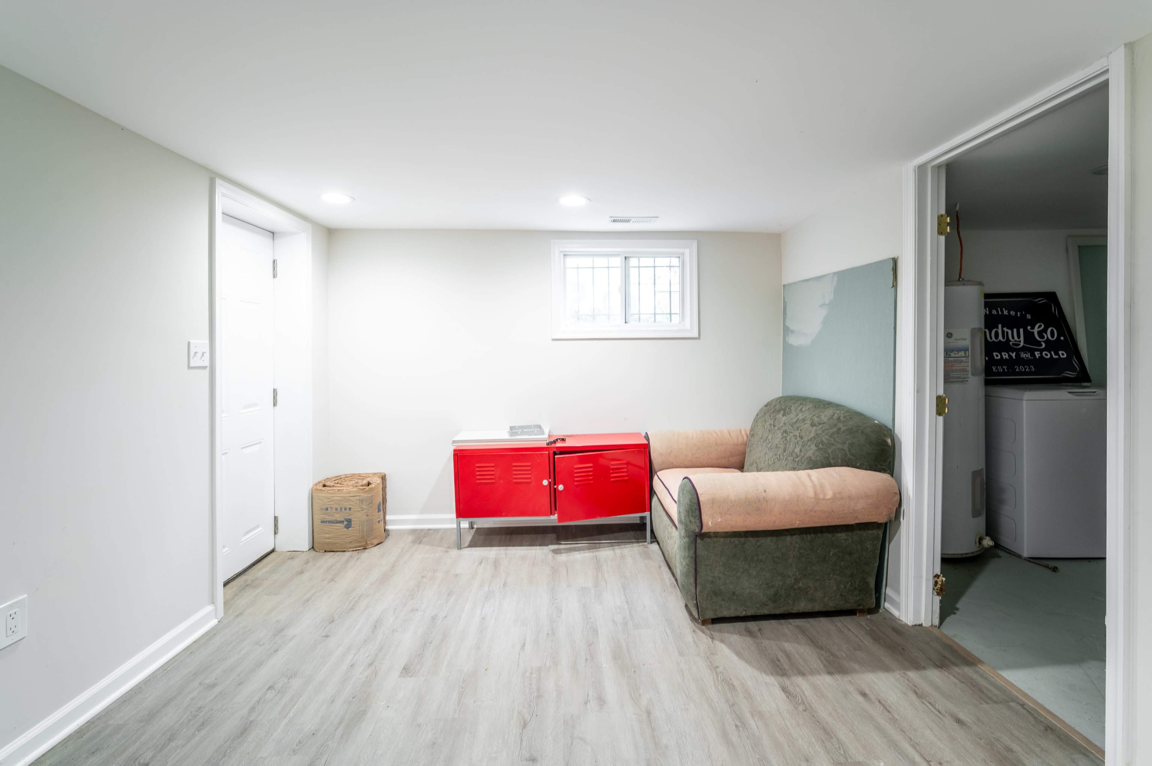 A small, unfinished basement features a green couch, a red cabinet, and a door leading to another room.