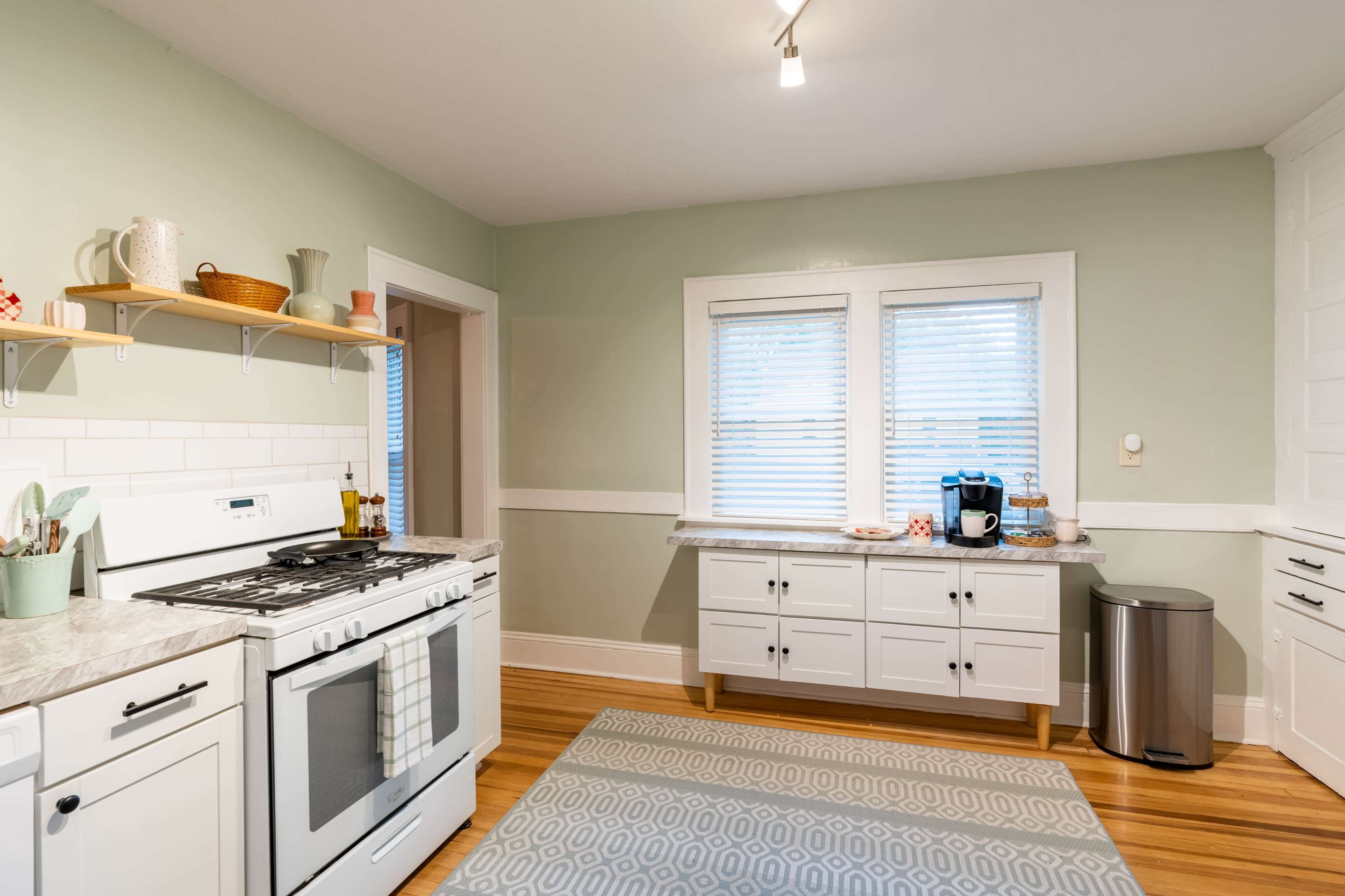 A modern kitchen with a gas stove, a light green wall, a countertop with a coffee maker, and wooden flooring.
