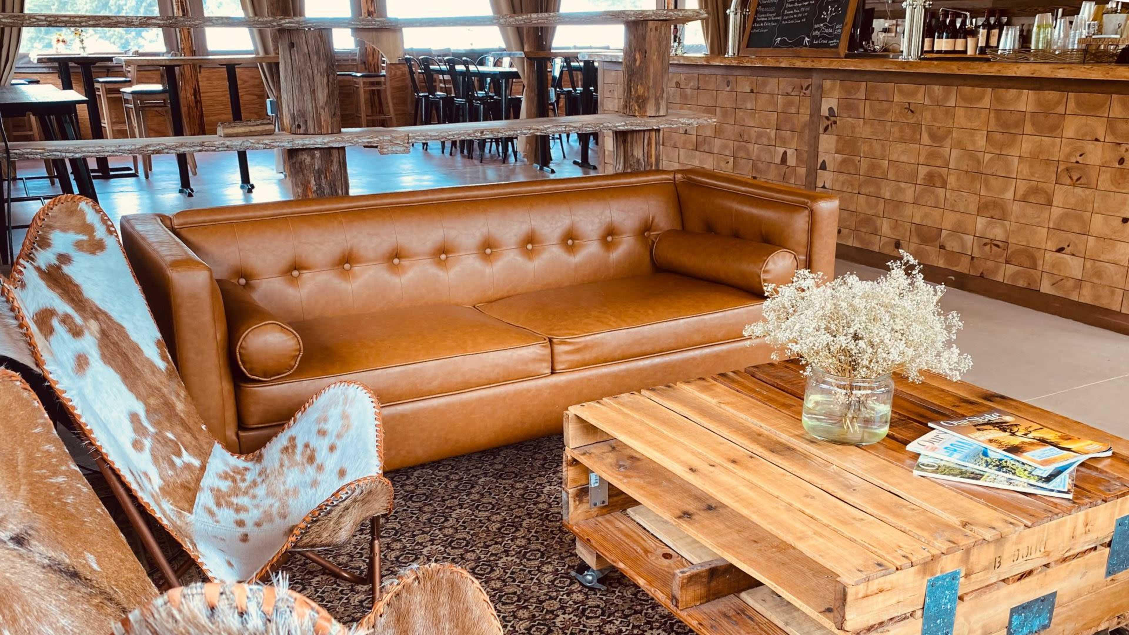 A rustic lounge area featuring a brown leather sofa, a wooden coffee table made from pallets, and a vase with flowers.