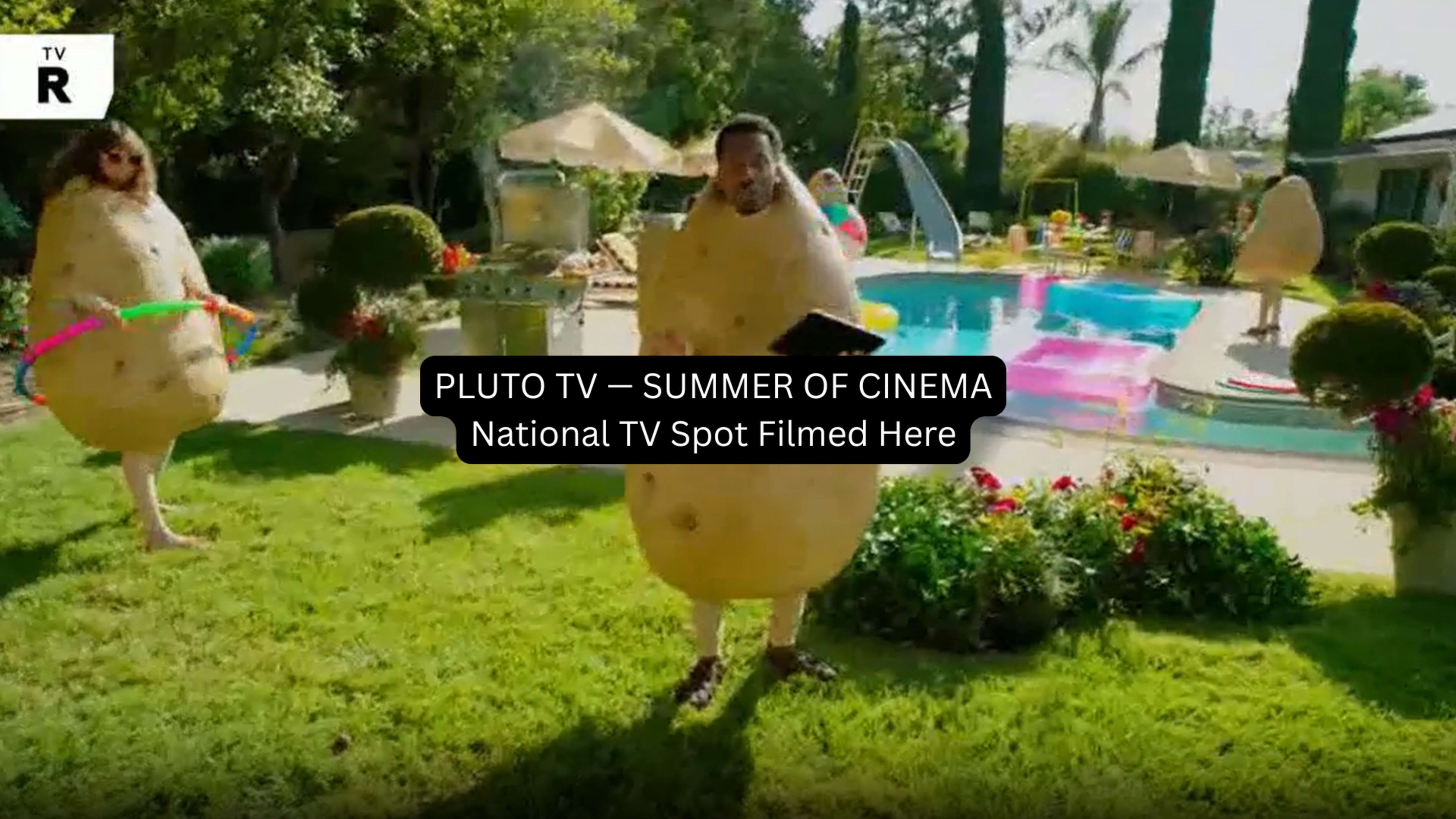 A person dressed in a potato costume stands in a backyard near a swimming pool, surrounded by greenery and colorful inflatable decorations.