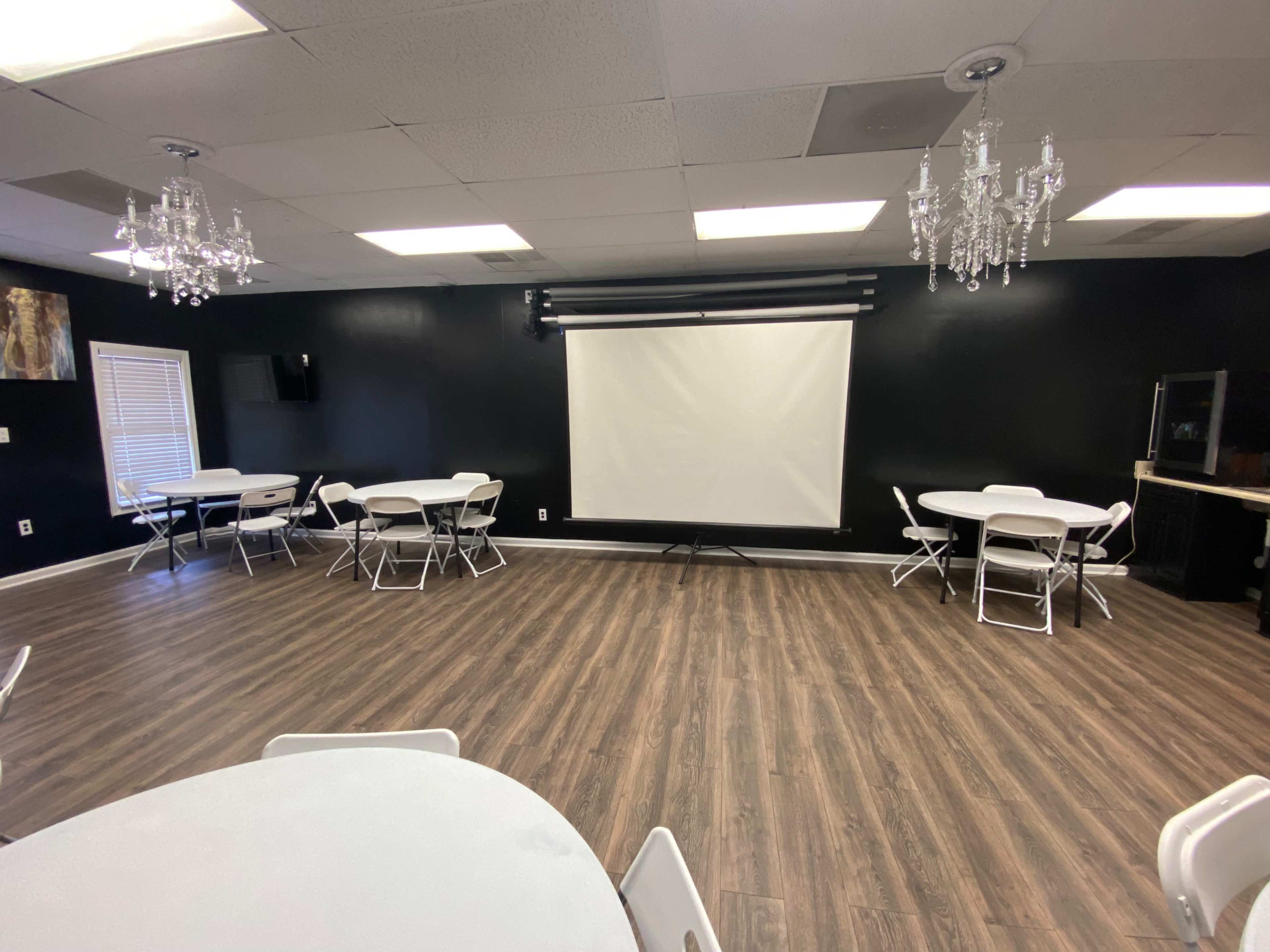 A spacious meeting room with black walls, several round tables, and a large screen for presentations.