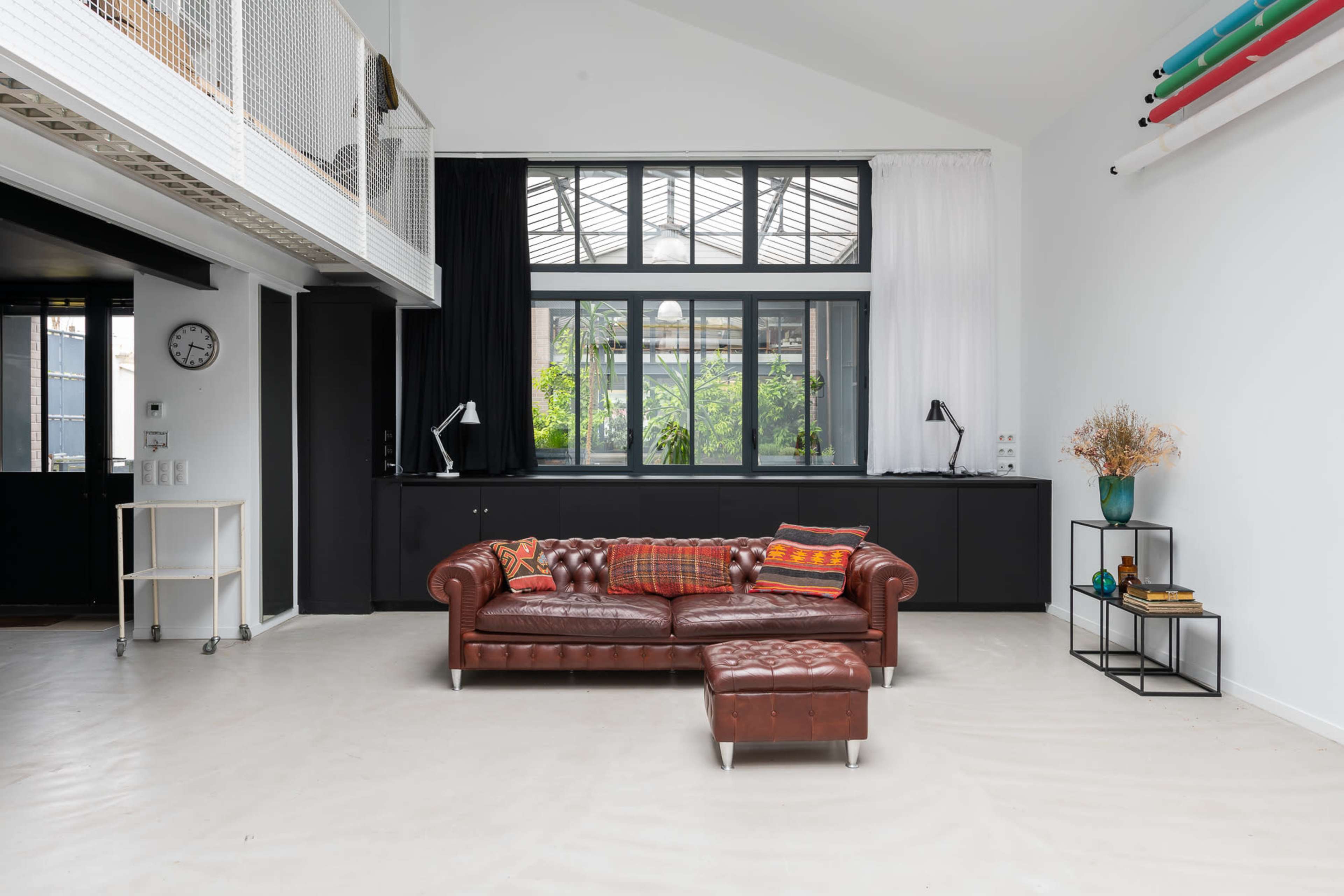 A spacious interior with a leather chesterfield sofa, a coffee table, and large windows overlooking greenery.