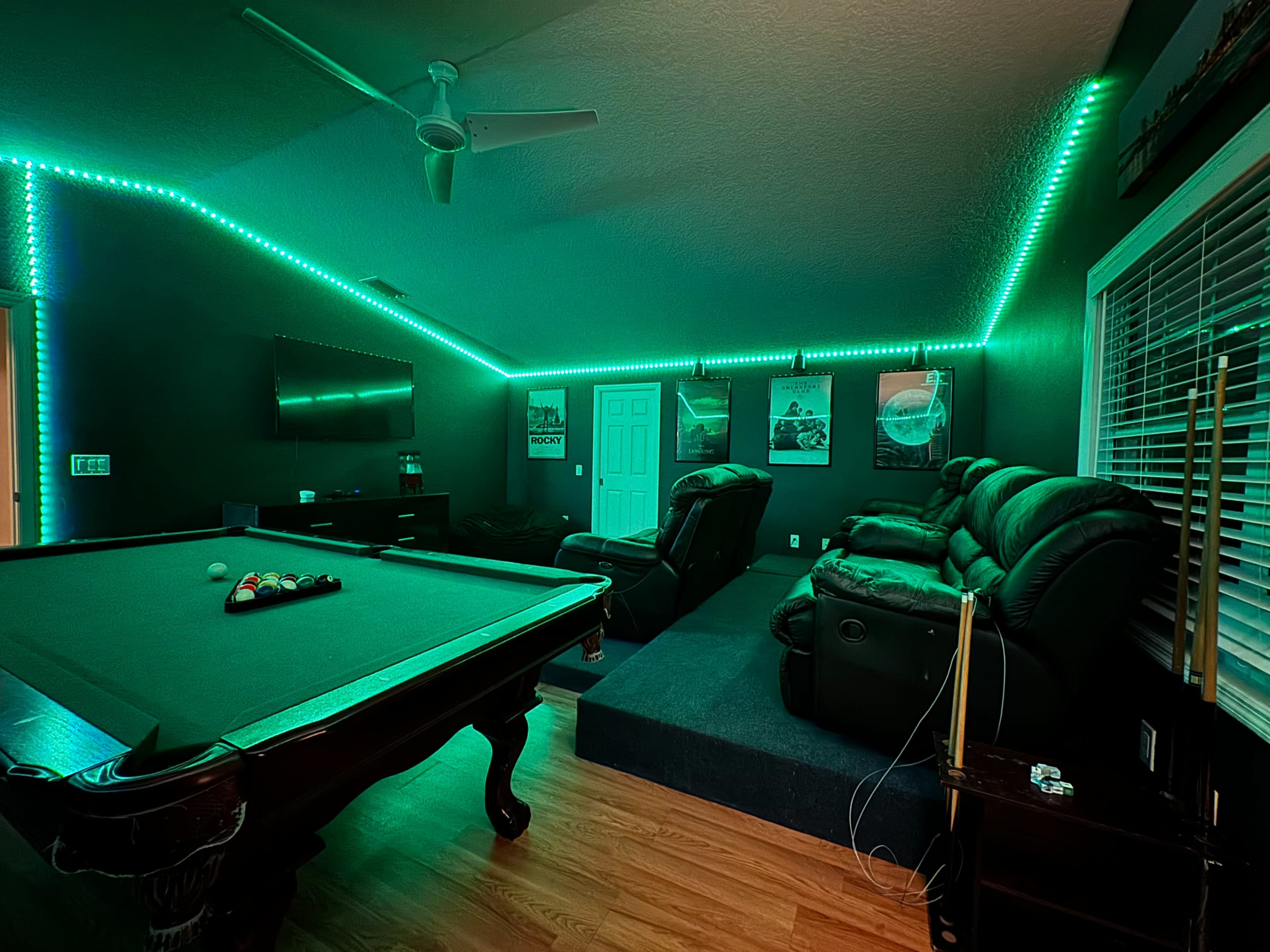The image shows a game room with a pool table, reclined seating, and ambient green LED lighting along the walls.