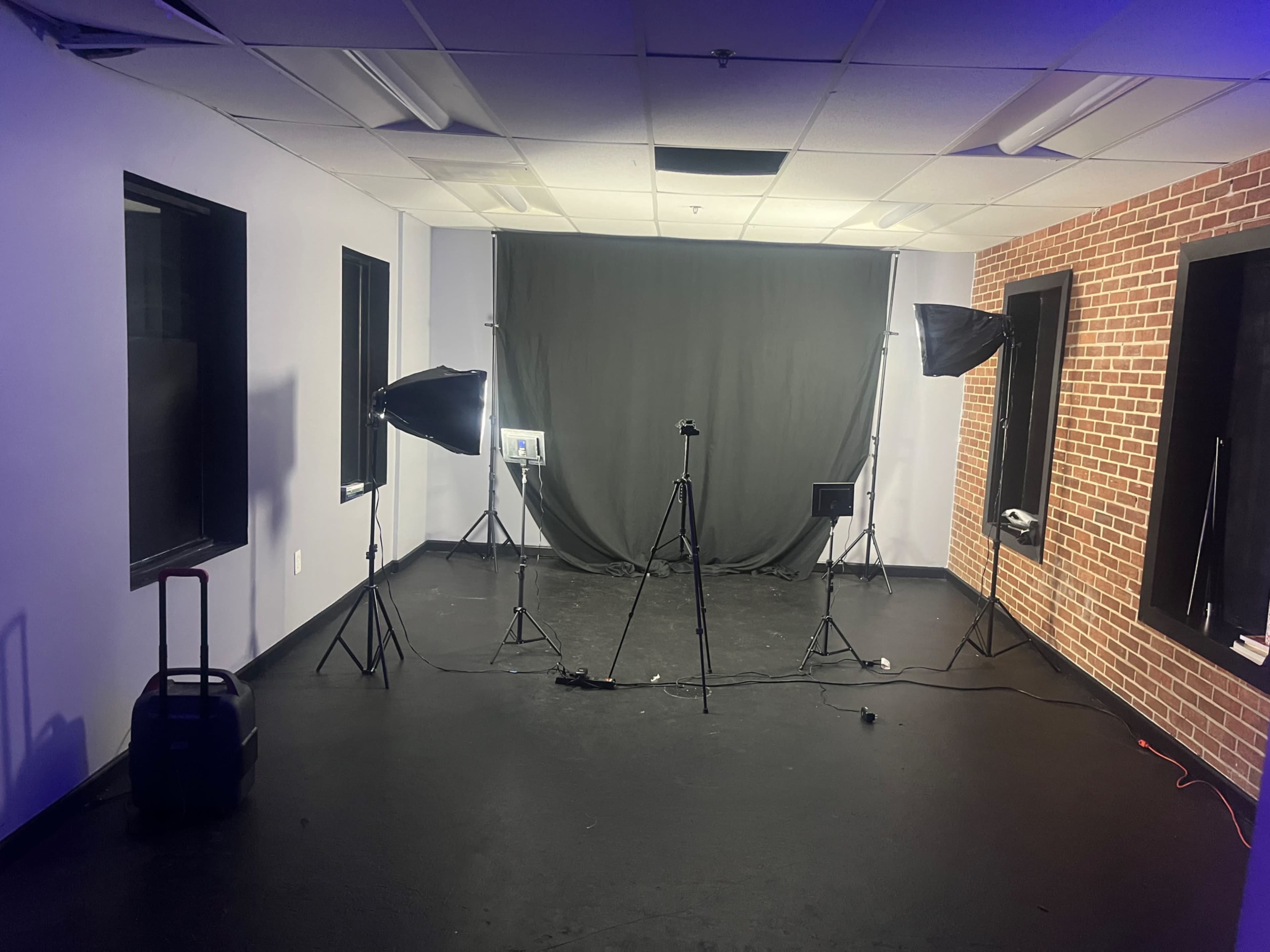 A photography studio setup with two light stands, a backdrop, and several tripods arranged on a dark floor.
