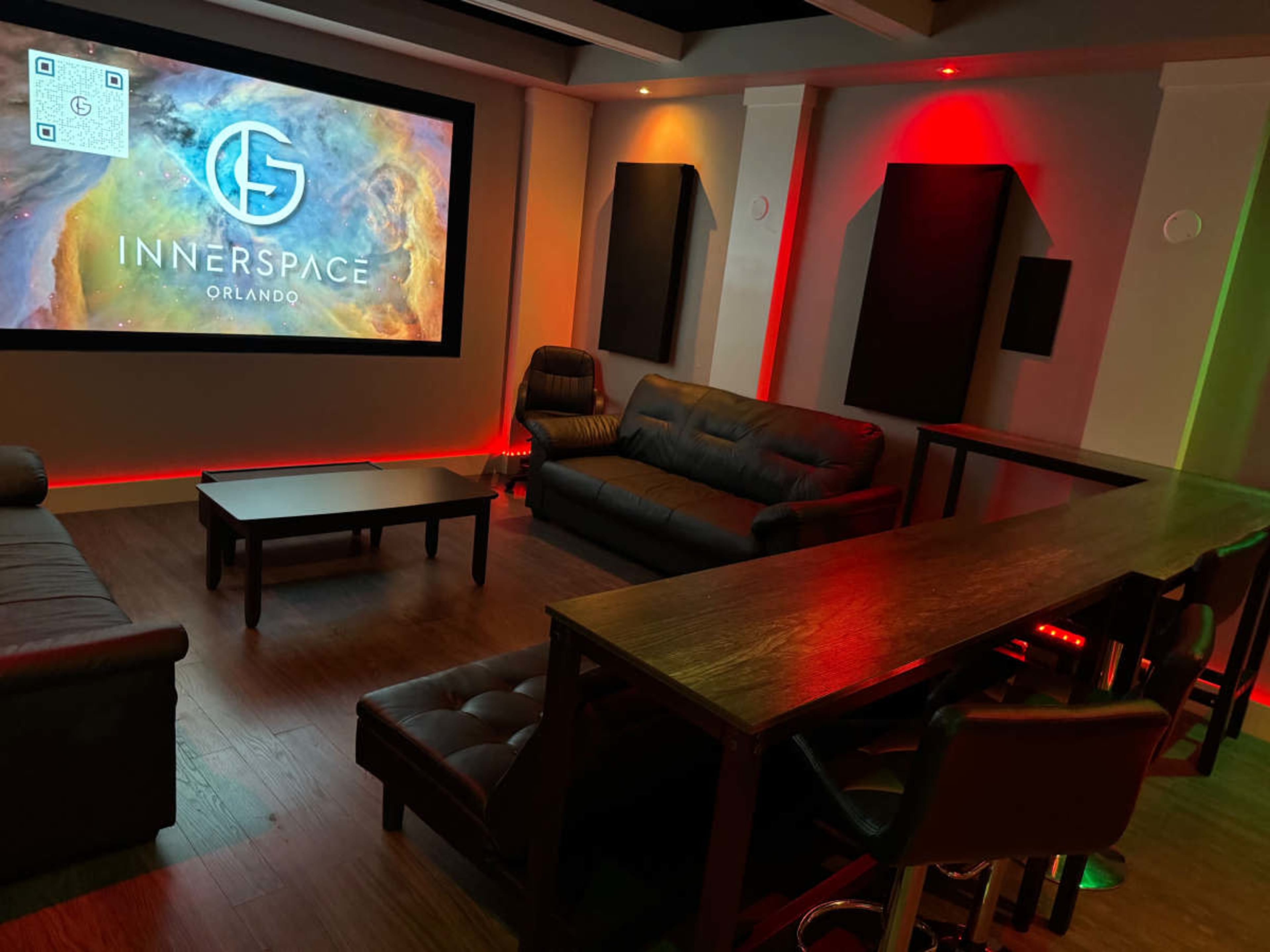 The image shows a modern lounge area featuring a large screen displaying "INNERSPACE ORLANDO," leather sofas, and a sleek bar counter with ambient lighting.