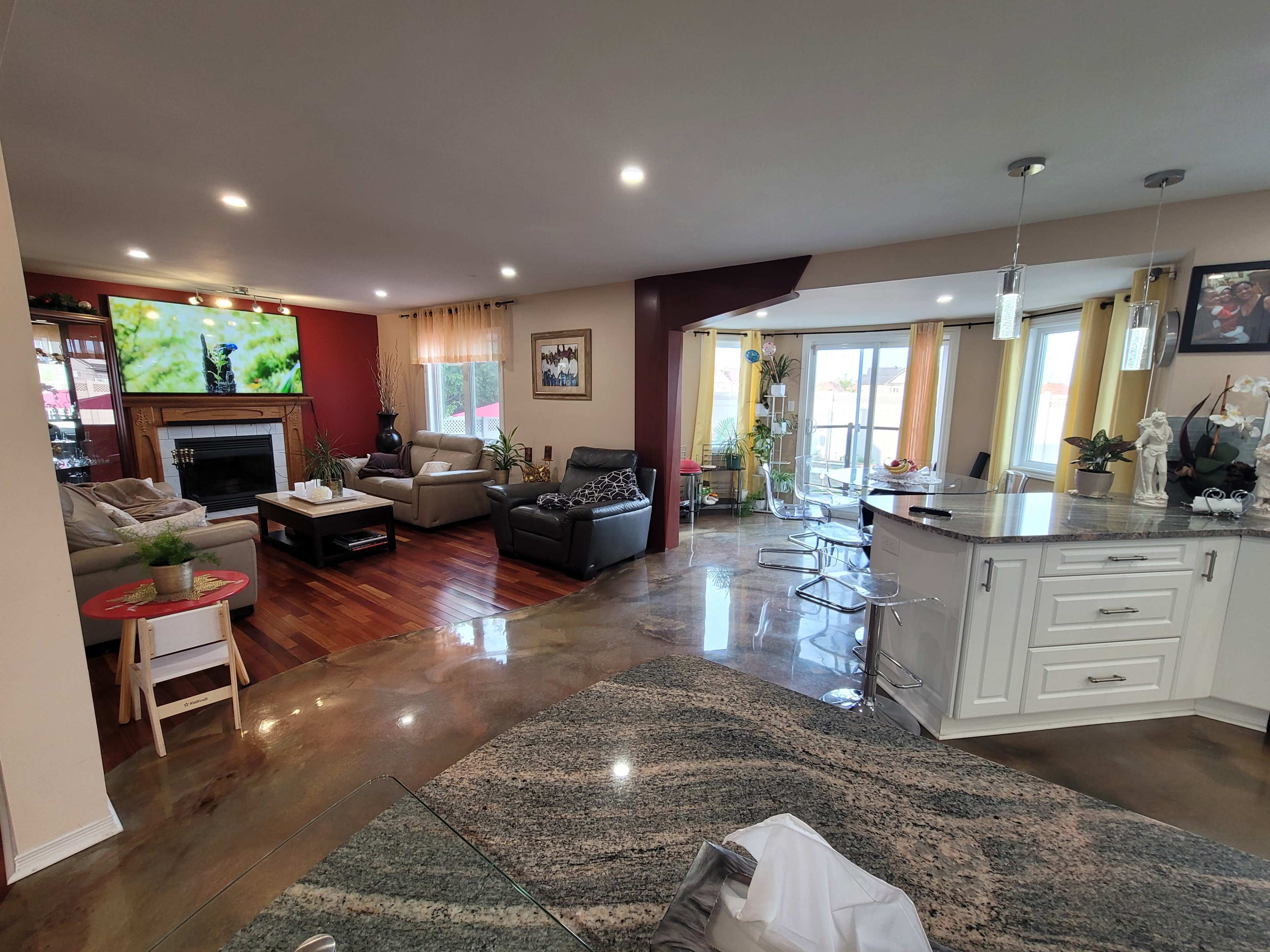 A spacious living area with a seating arrangement, a fireplace, and a kitchen bar featuring modern stools, all illuminated by natural light from large windows.