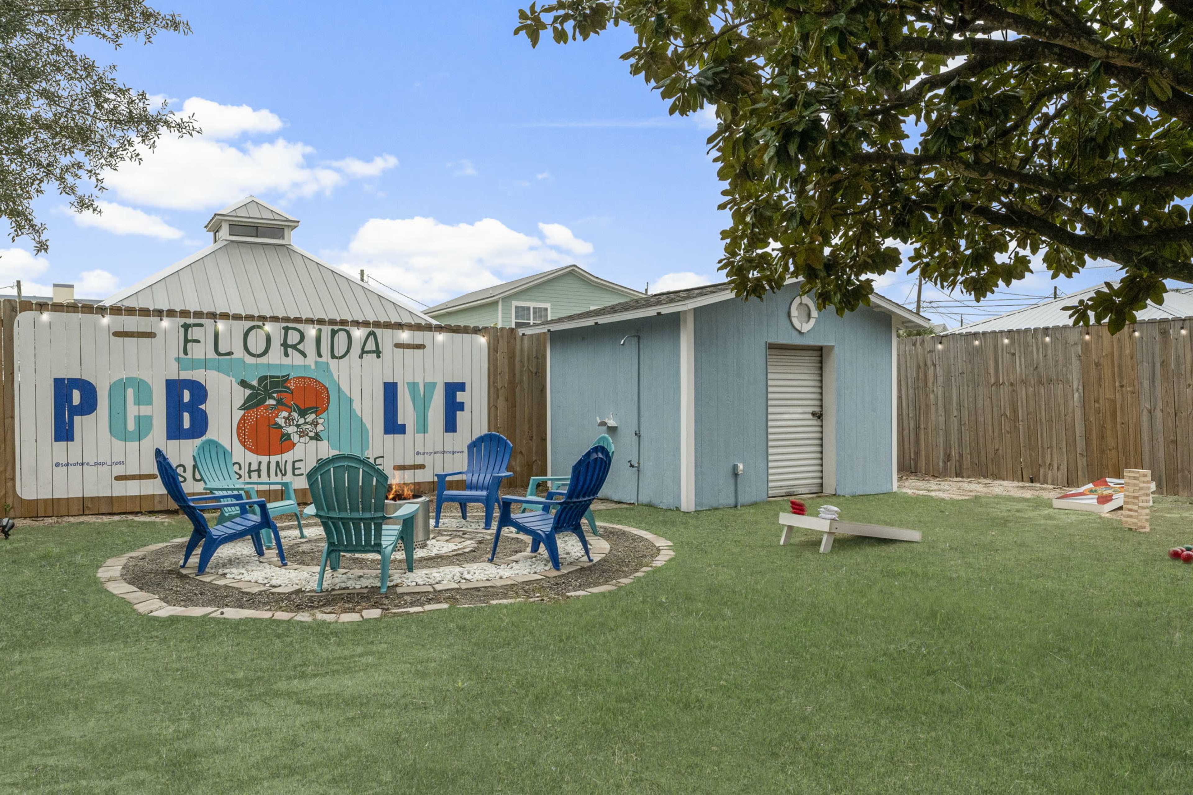 The image shows a backyard area in Florida with colorful chairs arranged around a stone circle, a shed in the background, and a large mural on the fence.