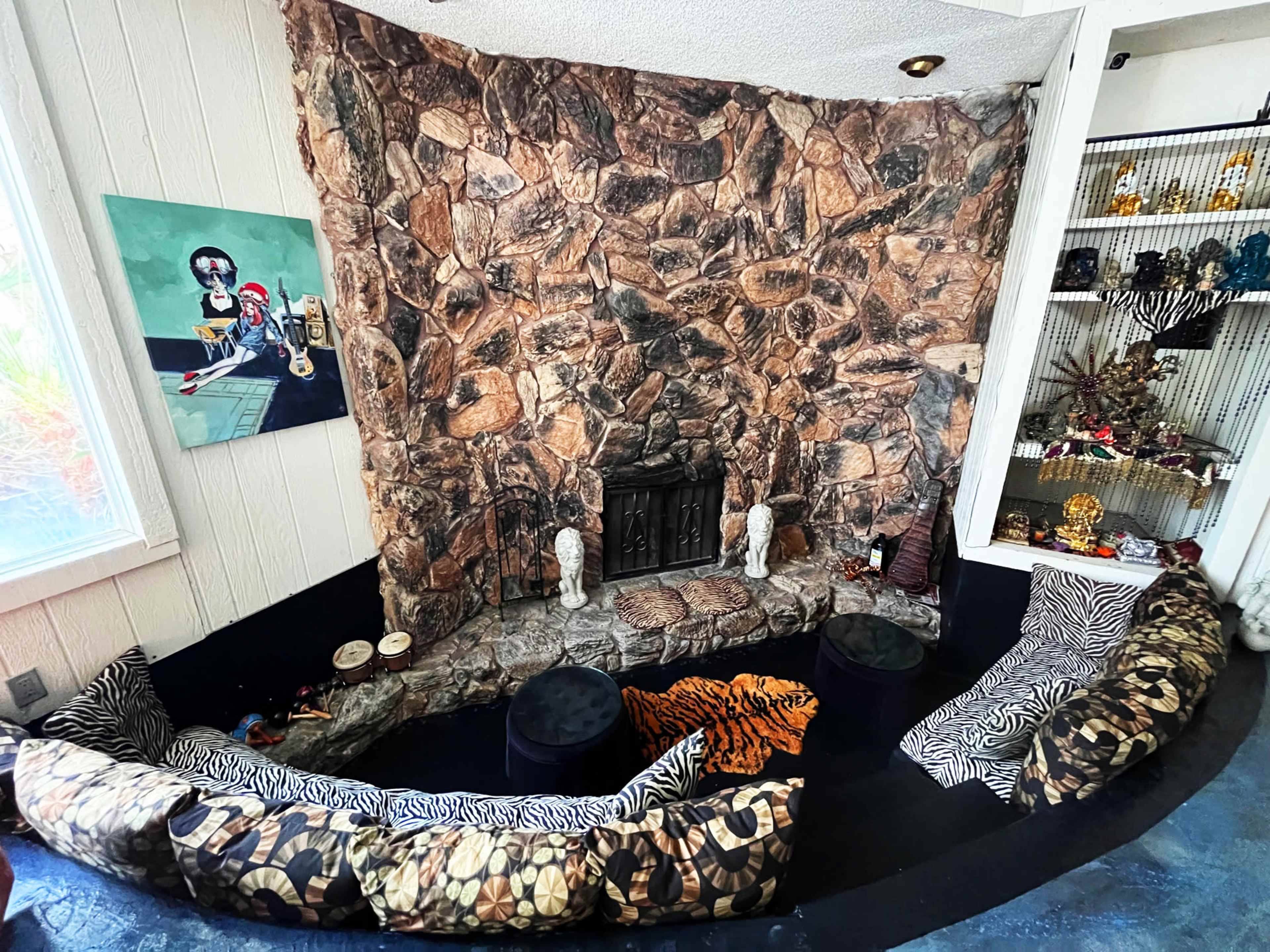 The image shows a cozy interior with a stone fireplace and a curved seating area adorned with animal-print cushions.