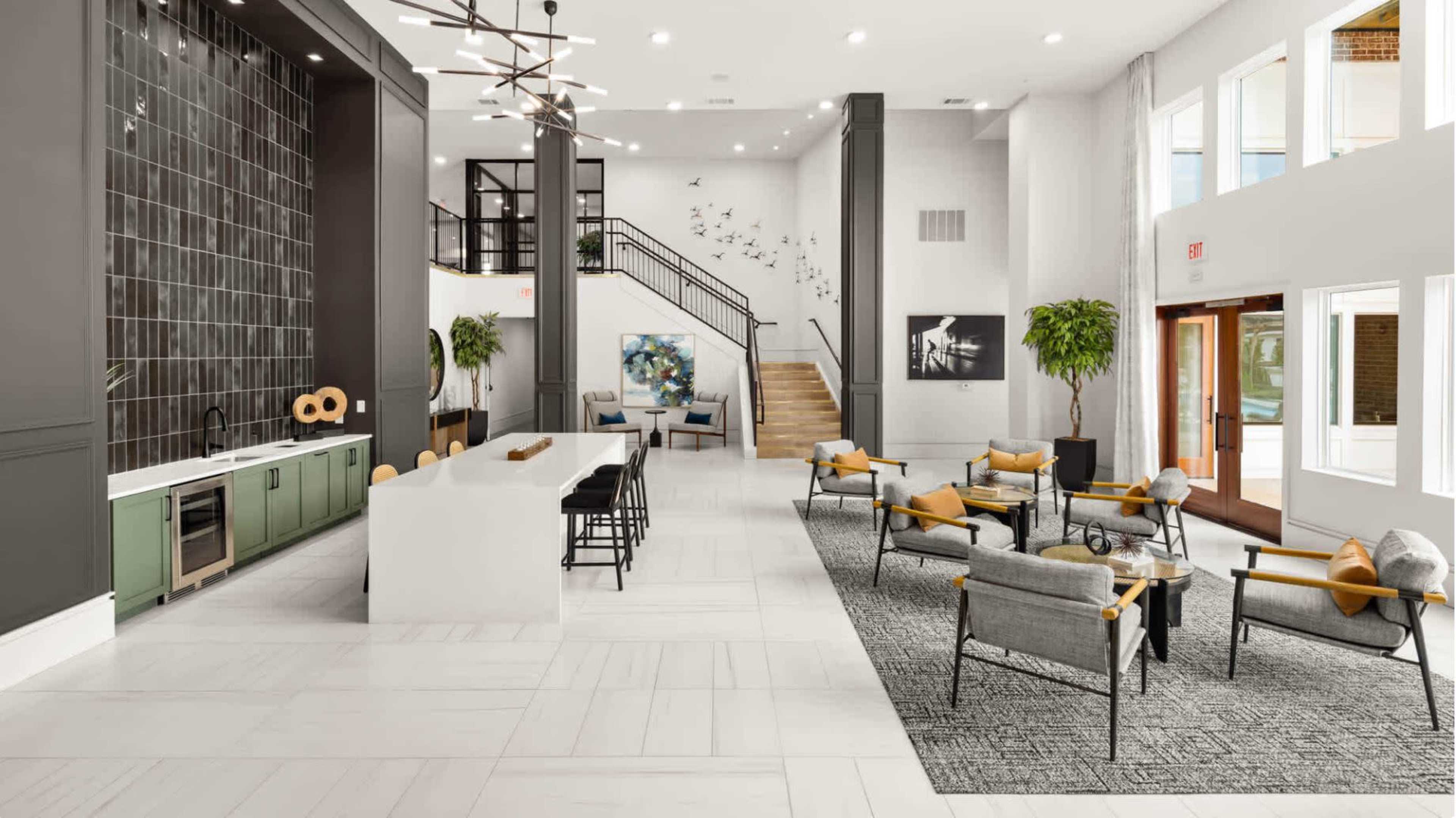 A modern lobby with a seating area, a kitchen counter, and a staircase leading to an upper level.