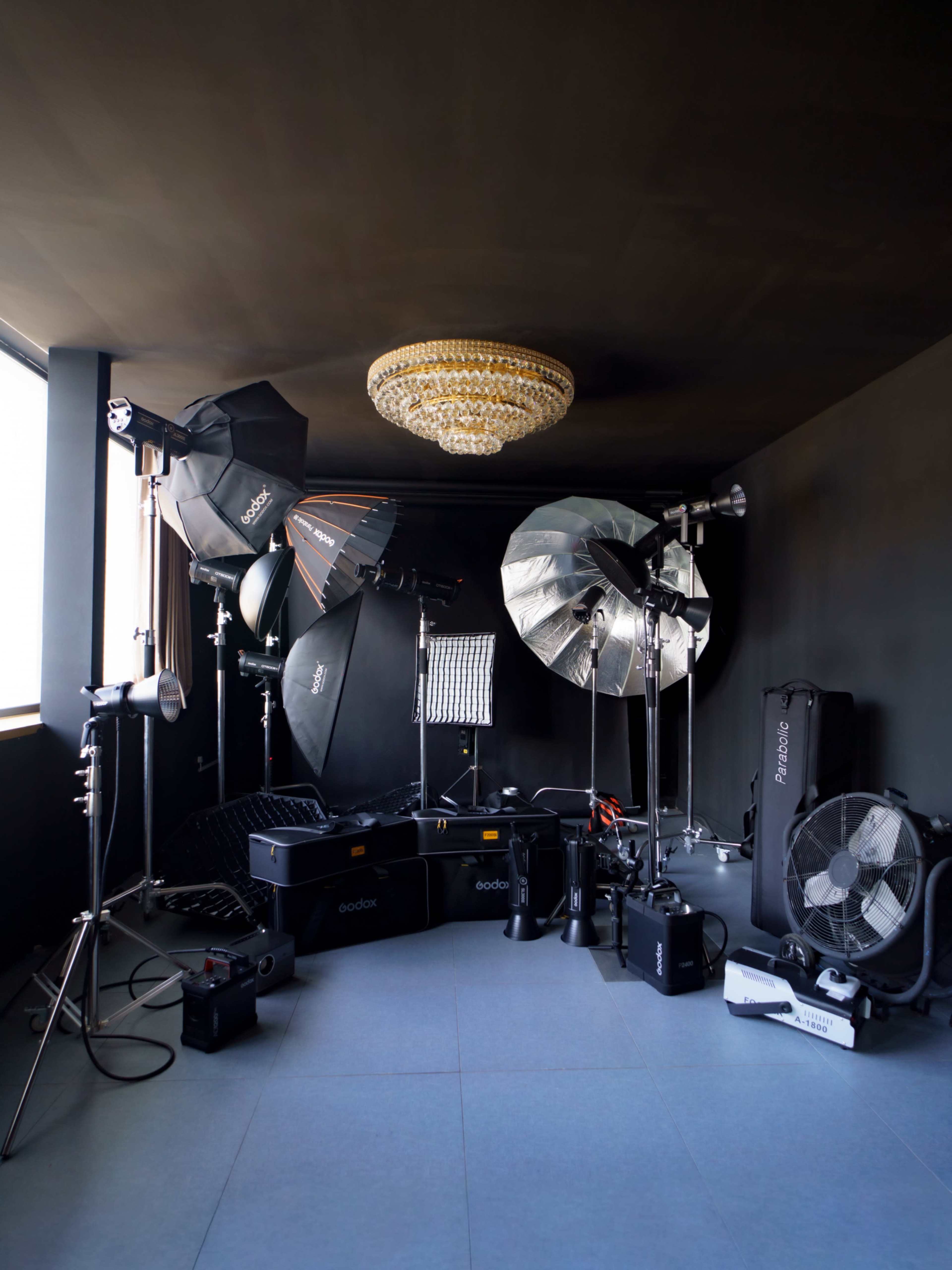 The image shows a photography studio equipped with various lighting equipment, including softboxes and stands, set against a dark wall.