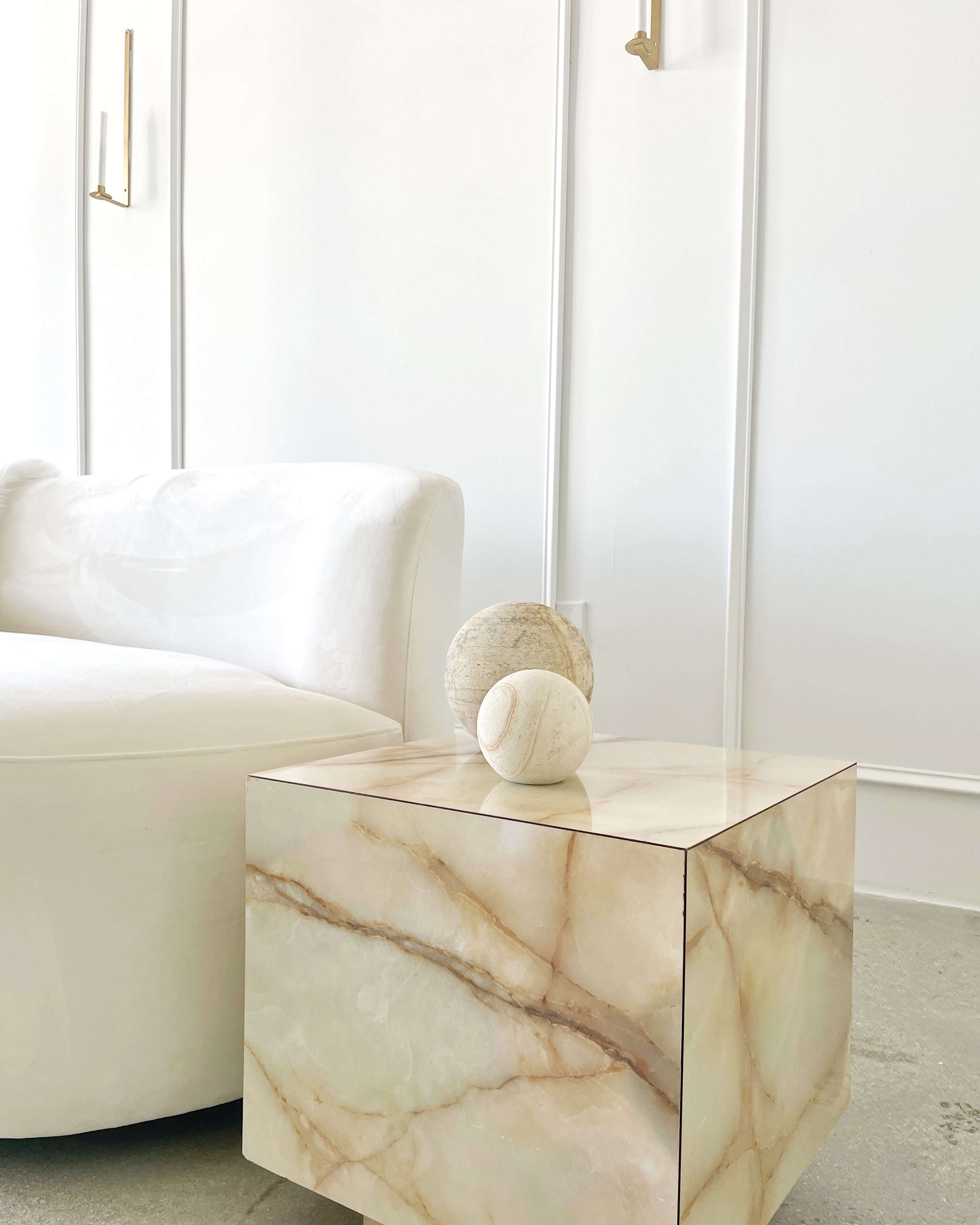 A smooth, light-colored couch is positioned next to a marble side table with two decorative stones on top.