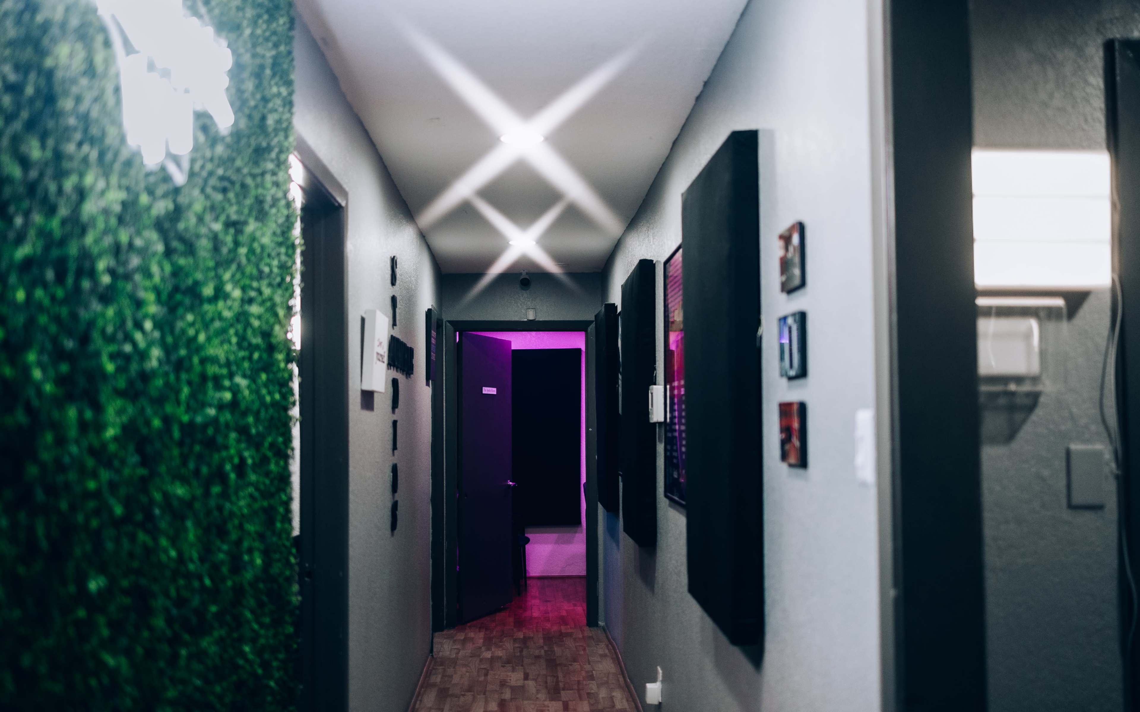 A narrow hallway with green wall accents, framed artworks, and purple lighting at the far end.