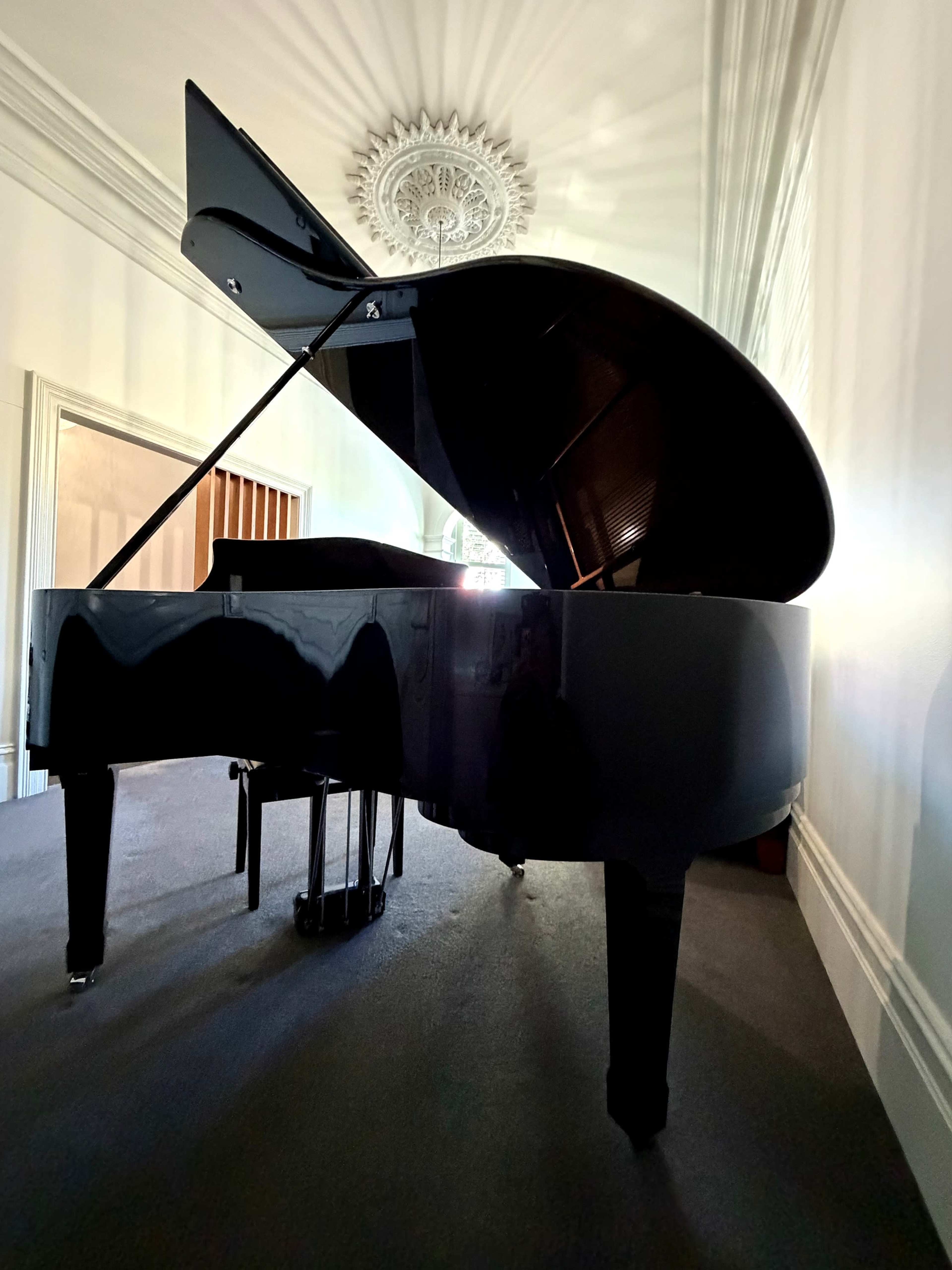 A grand piano is positioned in a room, showcasing its glossy black surface and an open lid that reveals the interior strings.