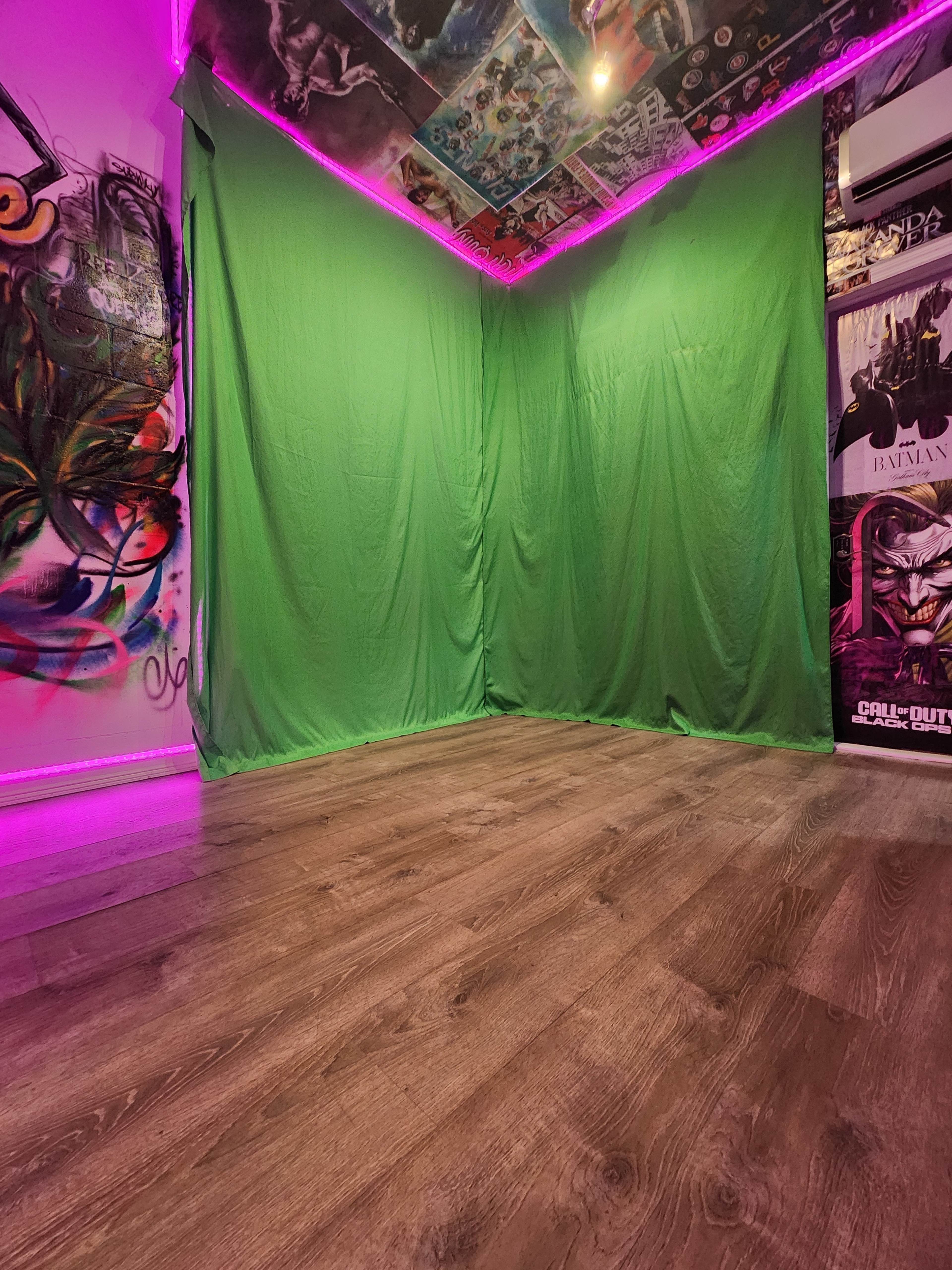 The image shows a room with green fabric covering the walls and ceiling, illuminated by pink lighting, and featuring wooden flooring.