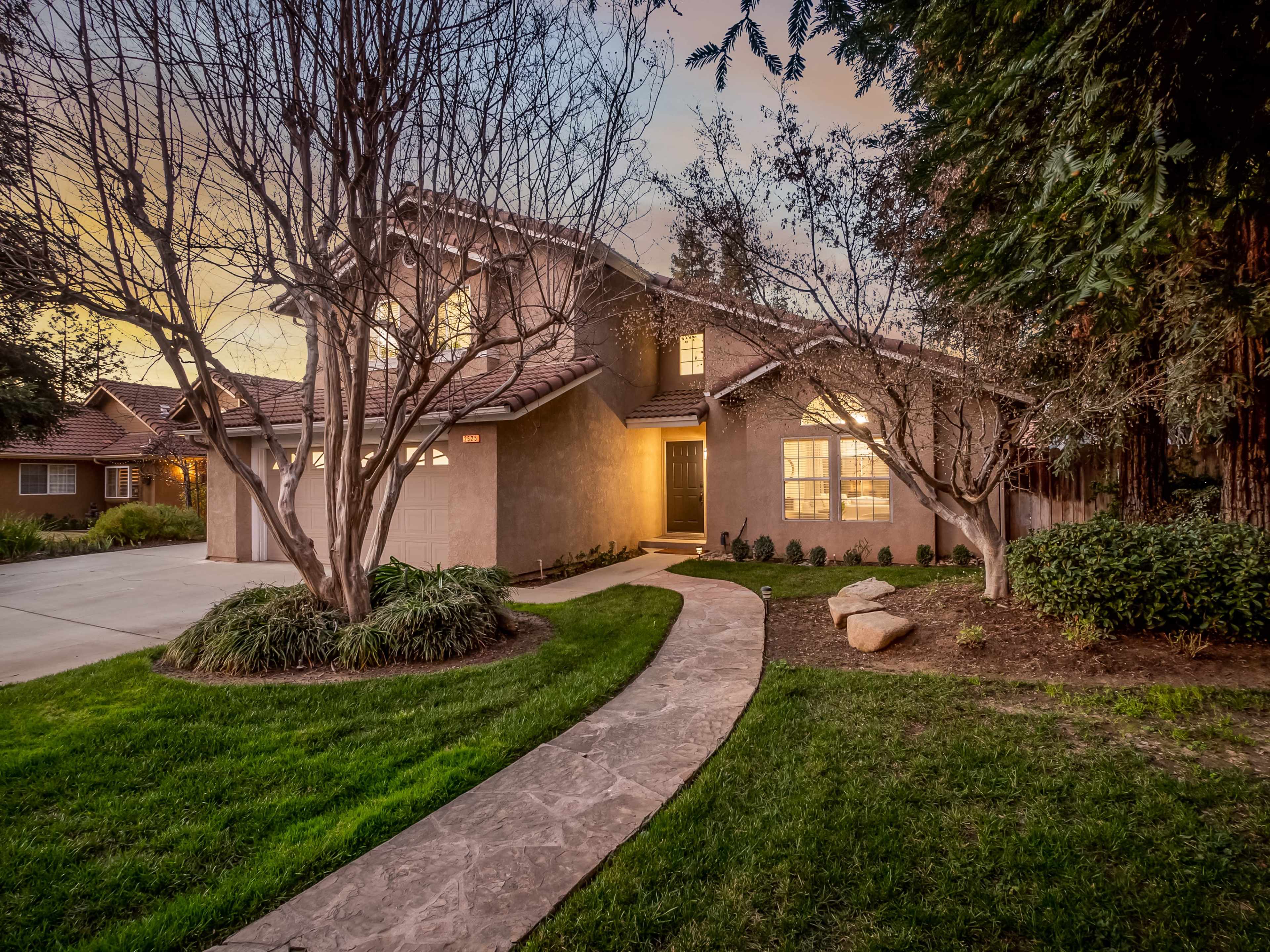 A two-story house with a landscaped front yard, a curved walkway, and a driveway leading to a garage.