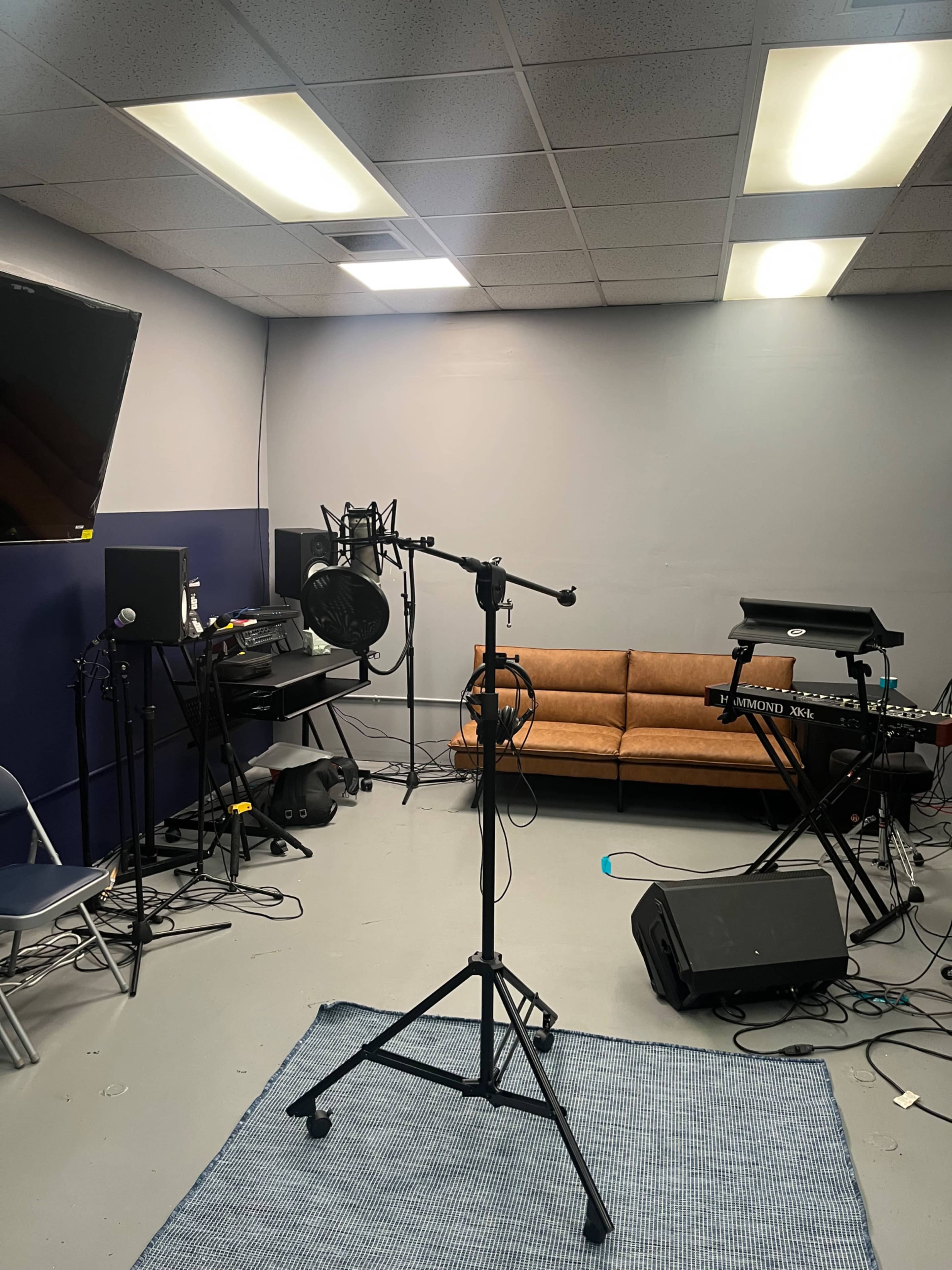 The image shows a small recording studio with a microphone on a stand, a couch, and various music equipment against the walls.