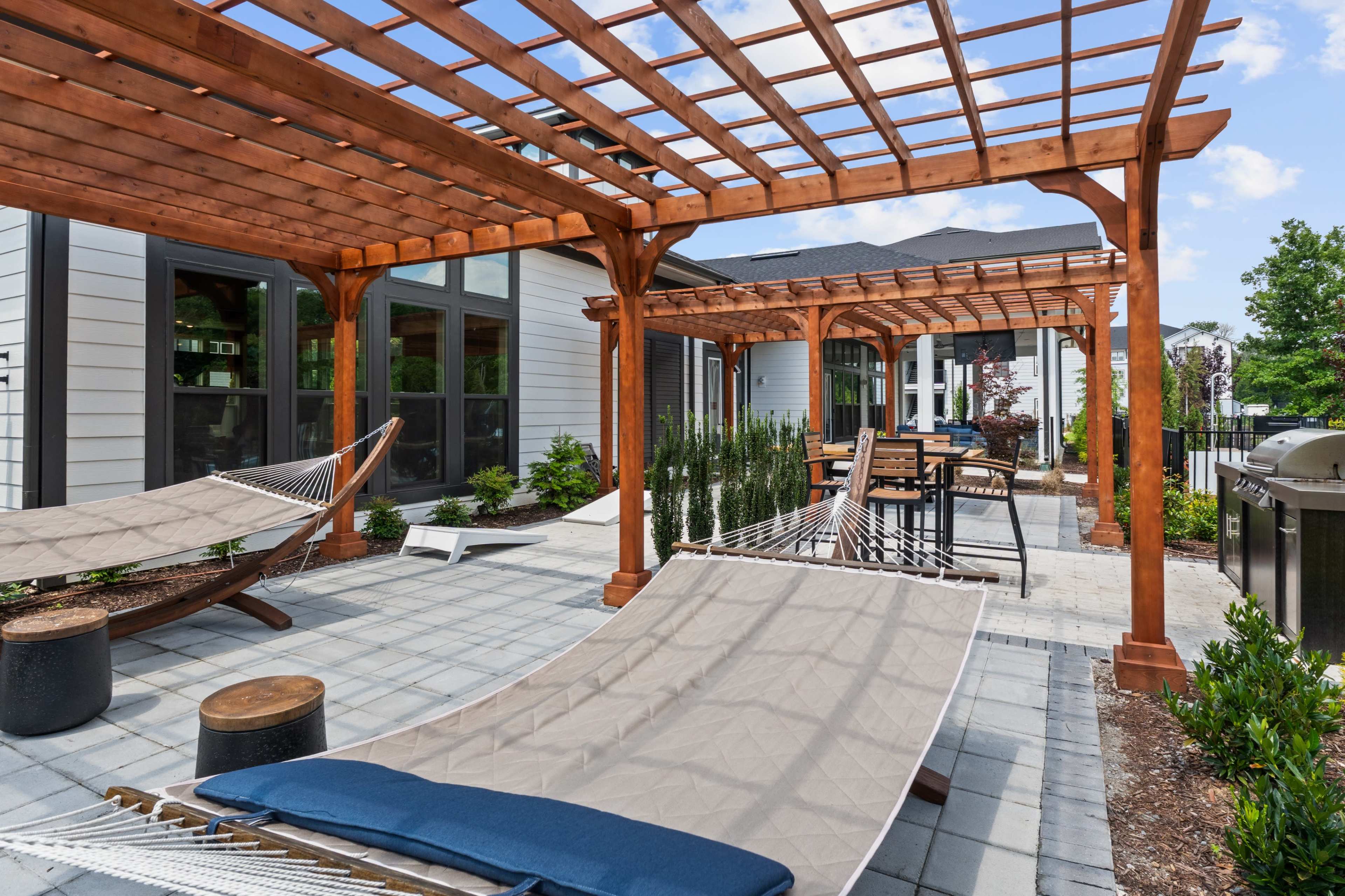 The image shows a patio area with wooden pergolas, hammocks, and outdoor furniture arranged on stone tiles.