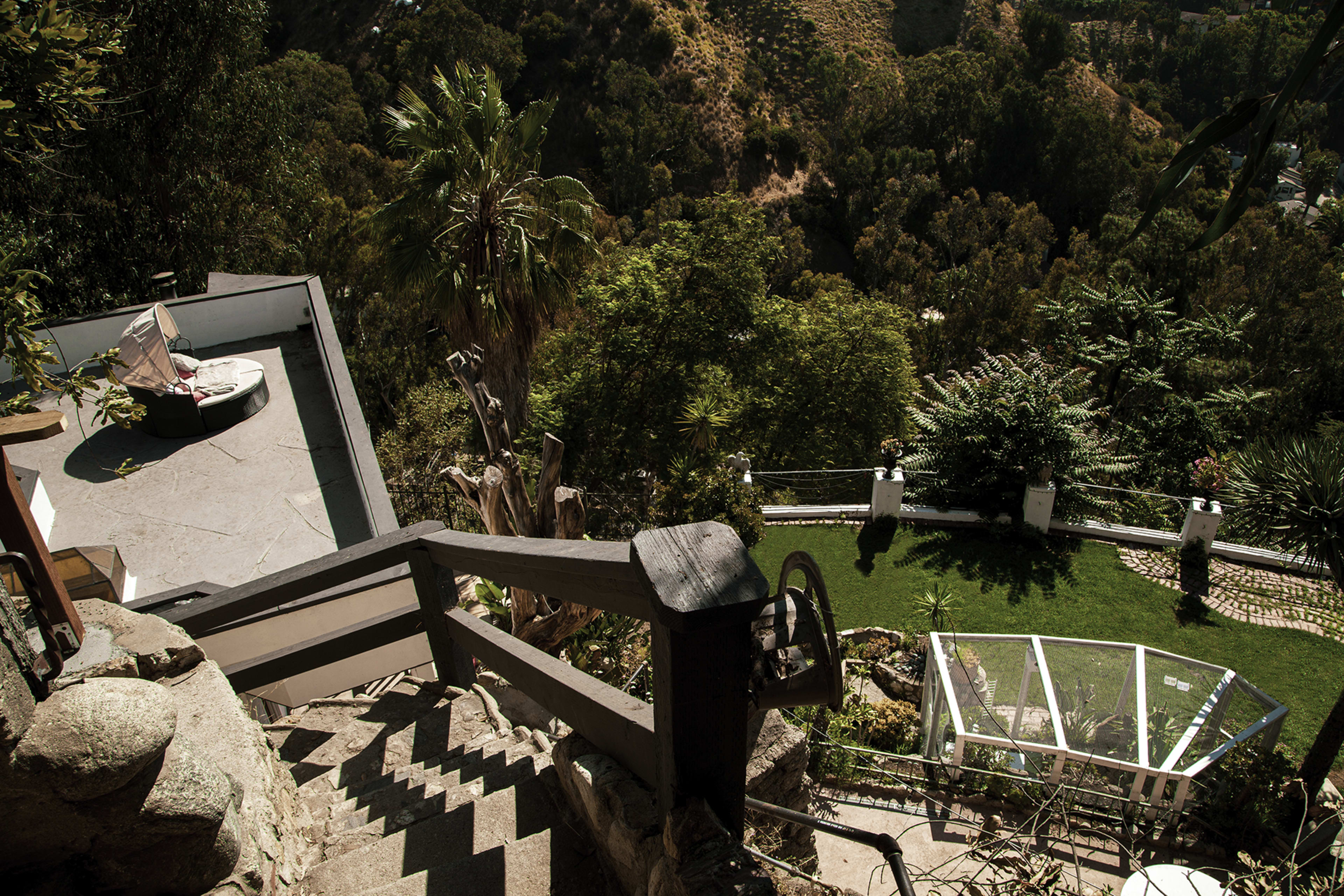 A winding stone staircase leading down to a landscaped area with a glass structure and a pool surrounded by greenery.