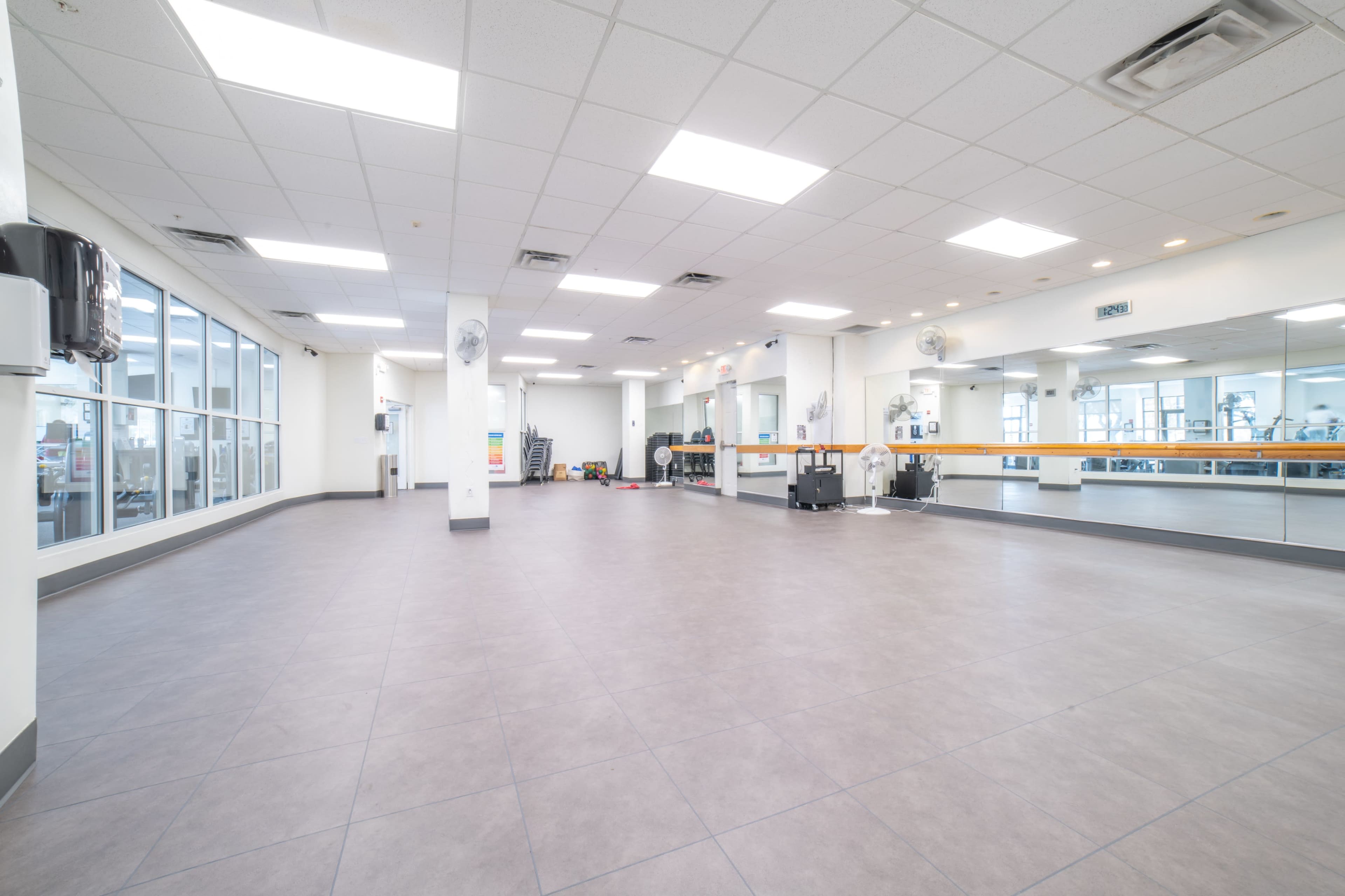 The image shows an empty exercise studio with large mirrors and a smooth tiled floor.