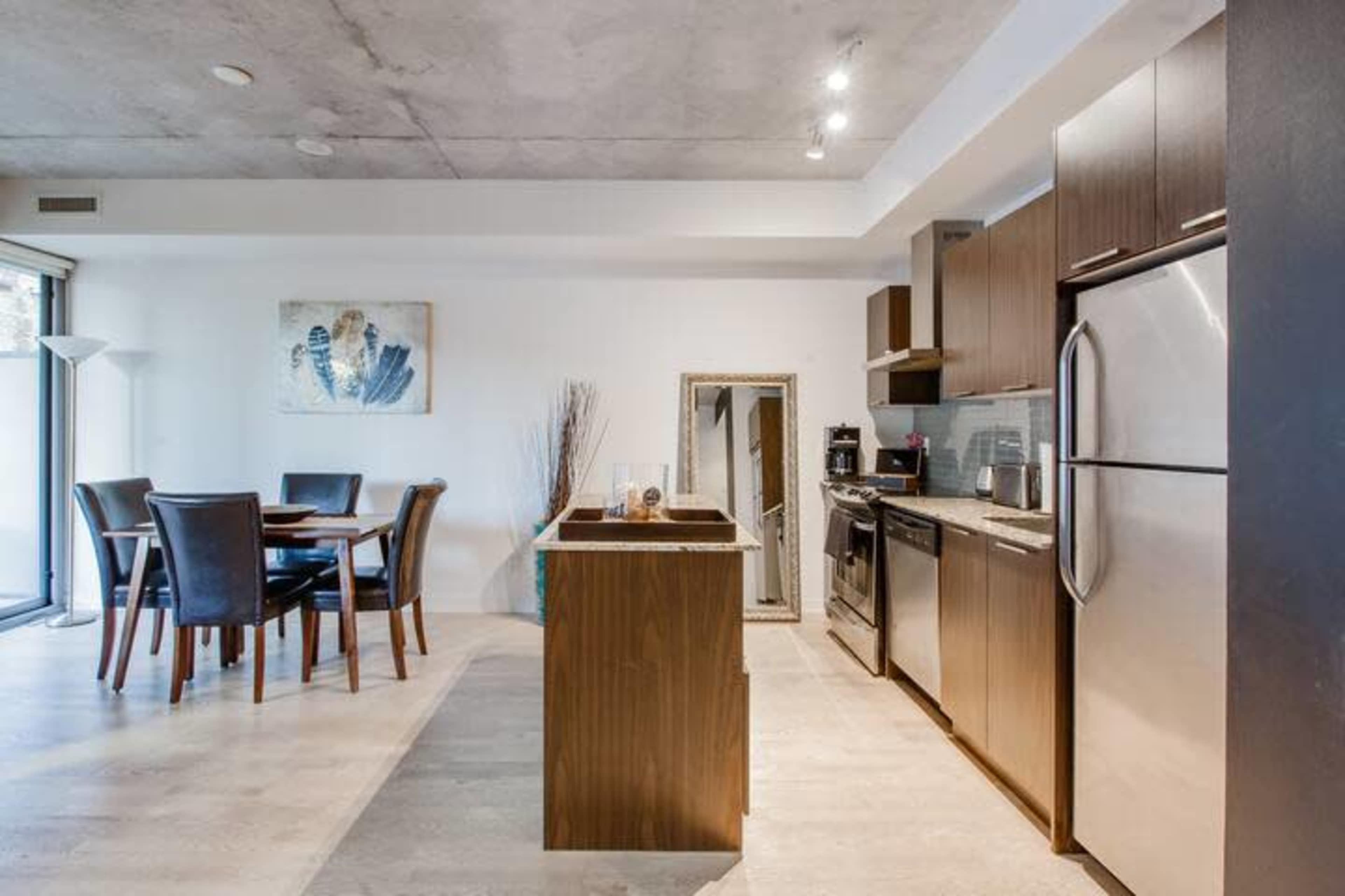A modern kitchen and dining area featuring a wooden dining table, black dining chairs, and stainless steel appliances.