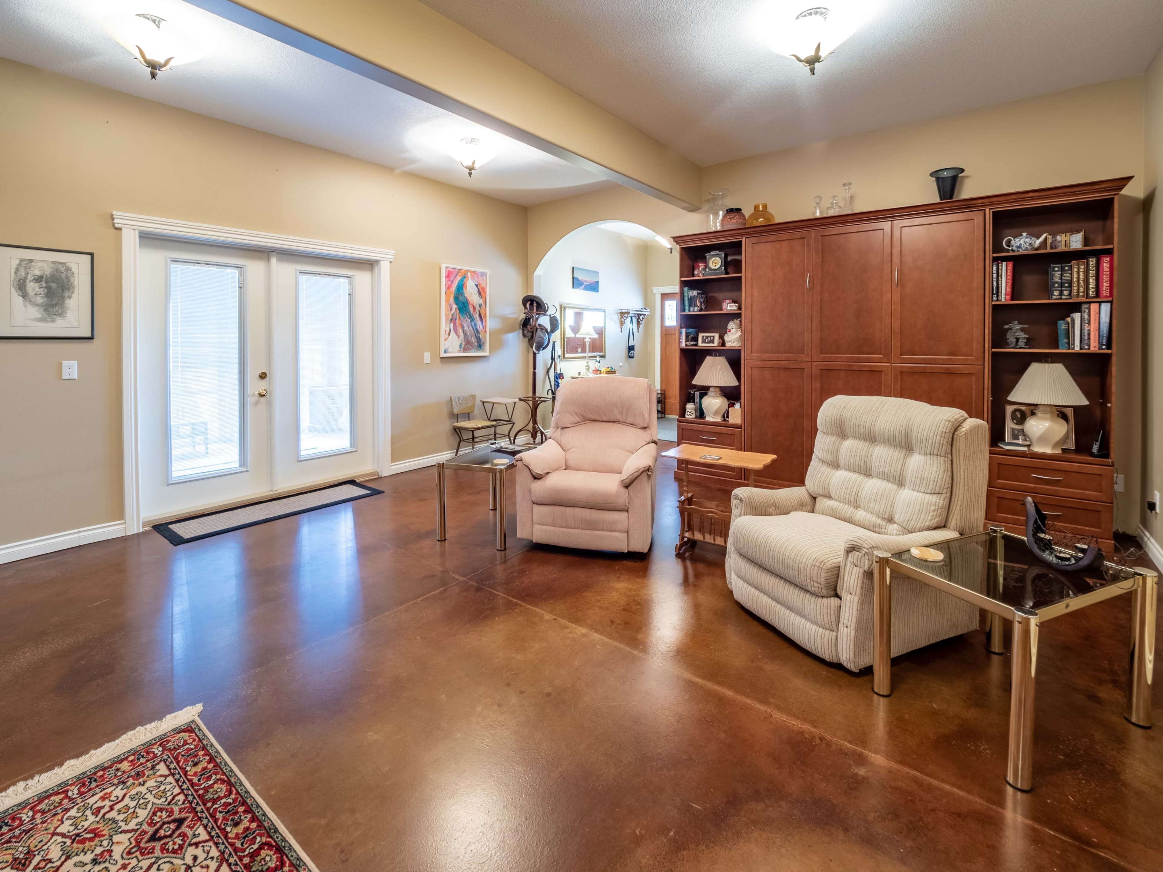 A spacious living area features light-colored walls, a reclining chair, and a wooden cabinet, with a view of sliding glass doors.