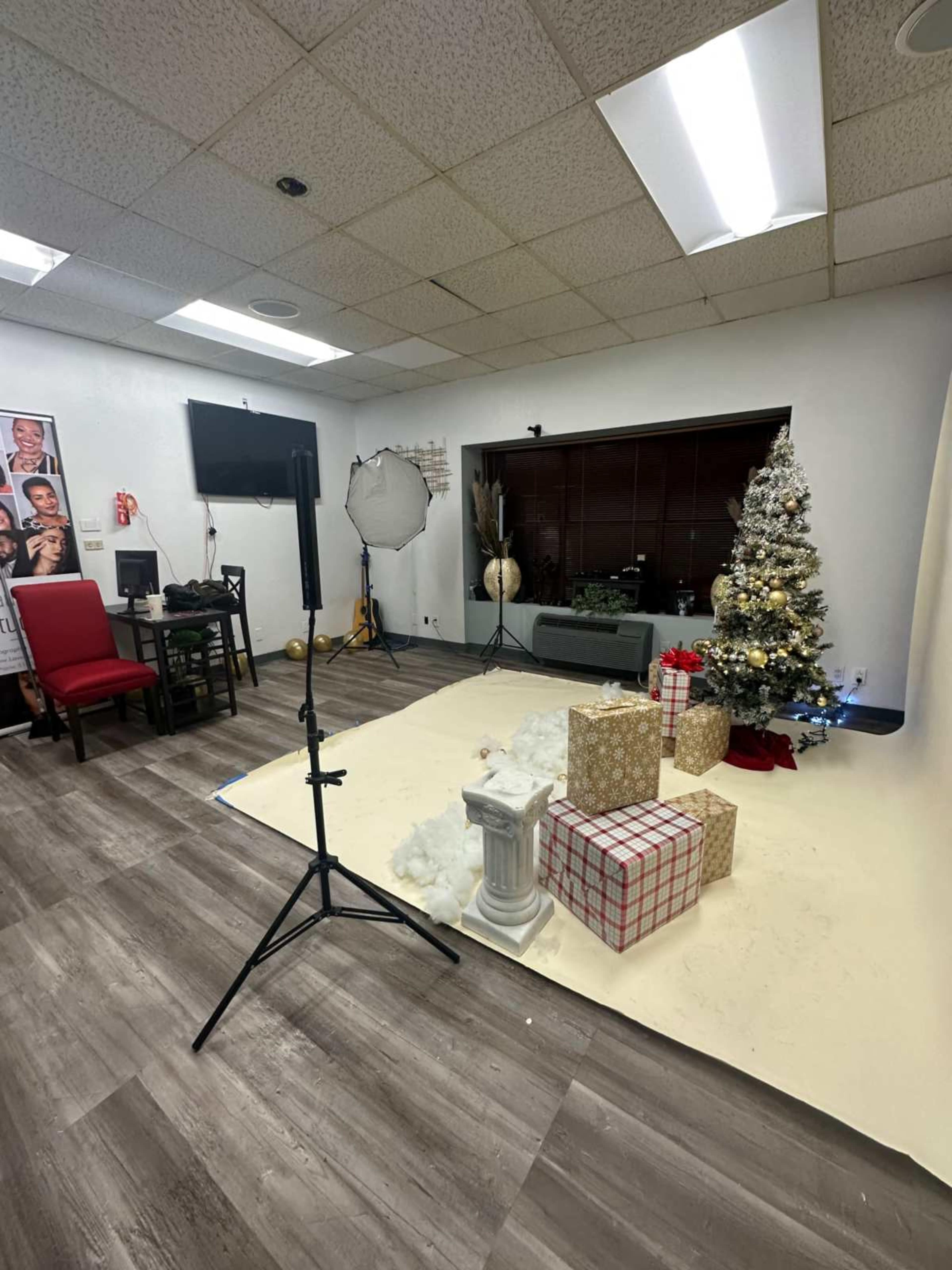 The image shows a photography studio decorated for the holidays, featuring a Christmas tree, presents, and a backdrop with a white floor.