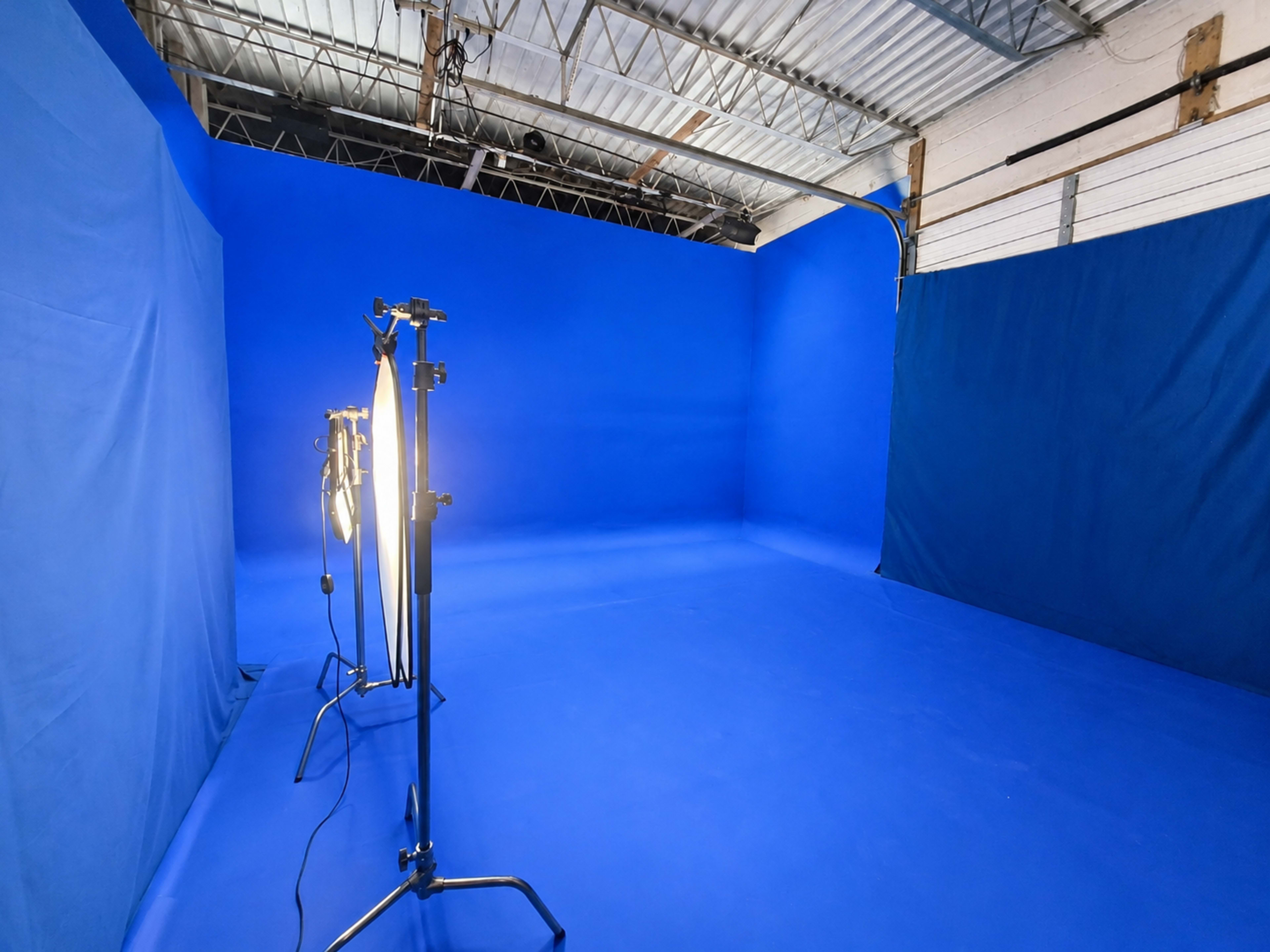 The image shows a spacious photo studio with blue walls and flooring, equipped with lighting stands.