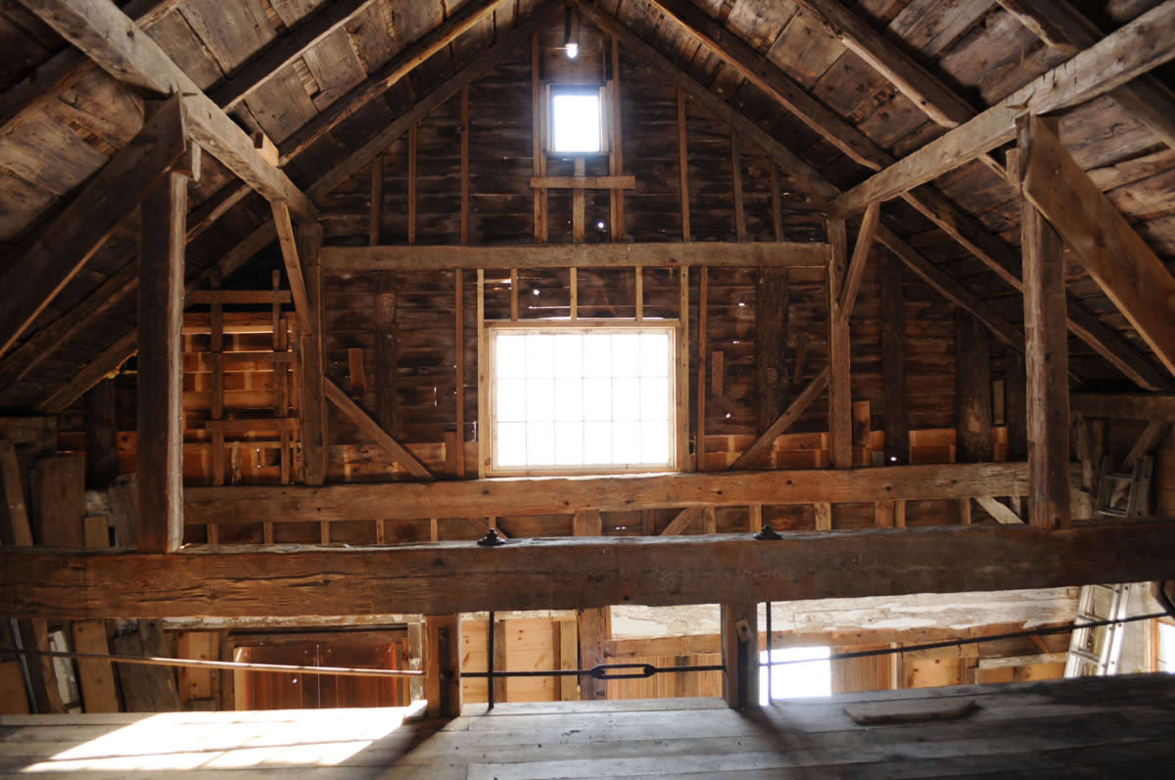 The interior of a rustic wooden barn with exposed beams and a large window at the center.