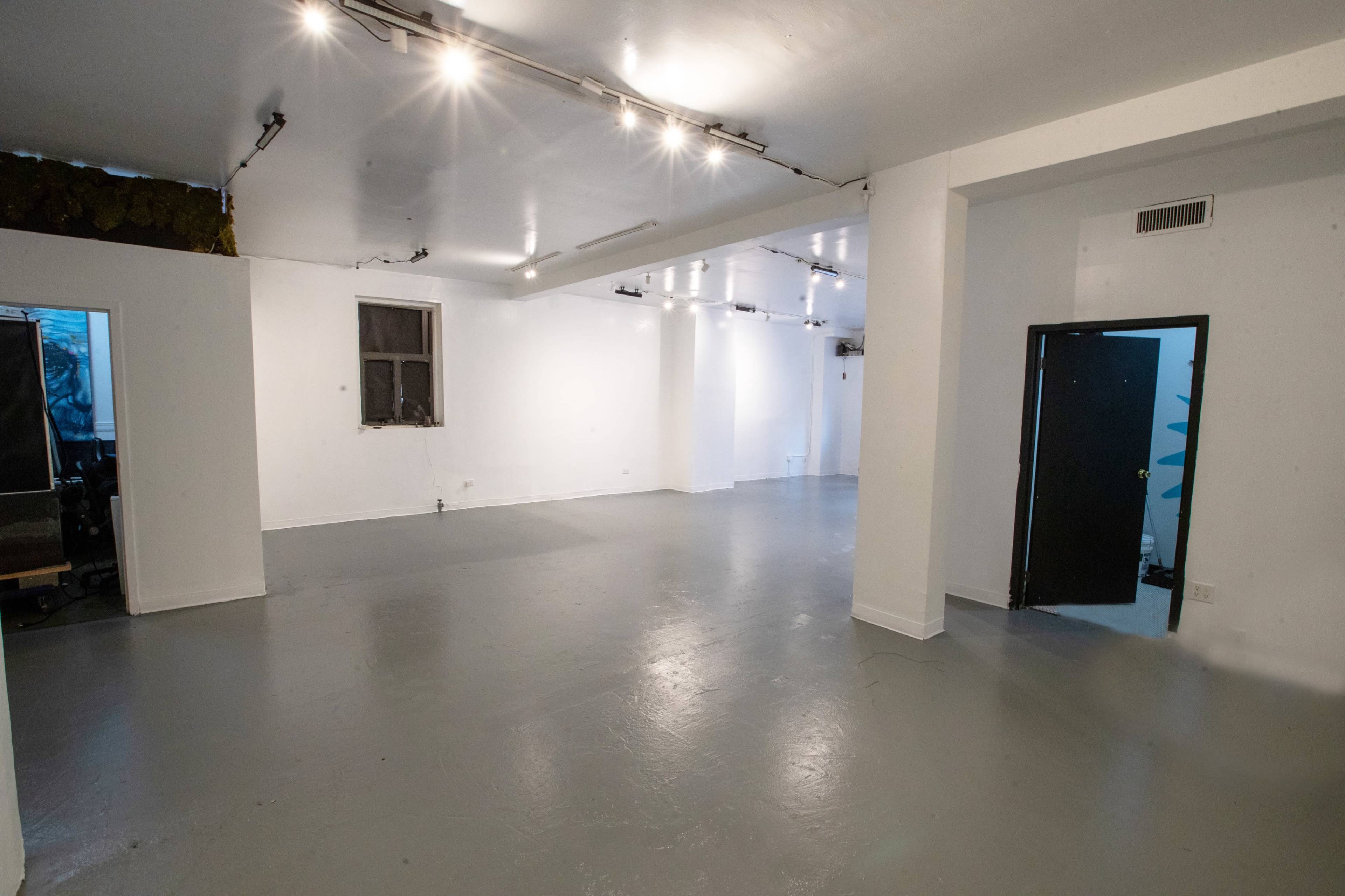 A spacious, empty room with polished gray flooring and white walls, illuminated by ceiling lights.