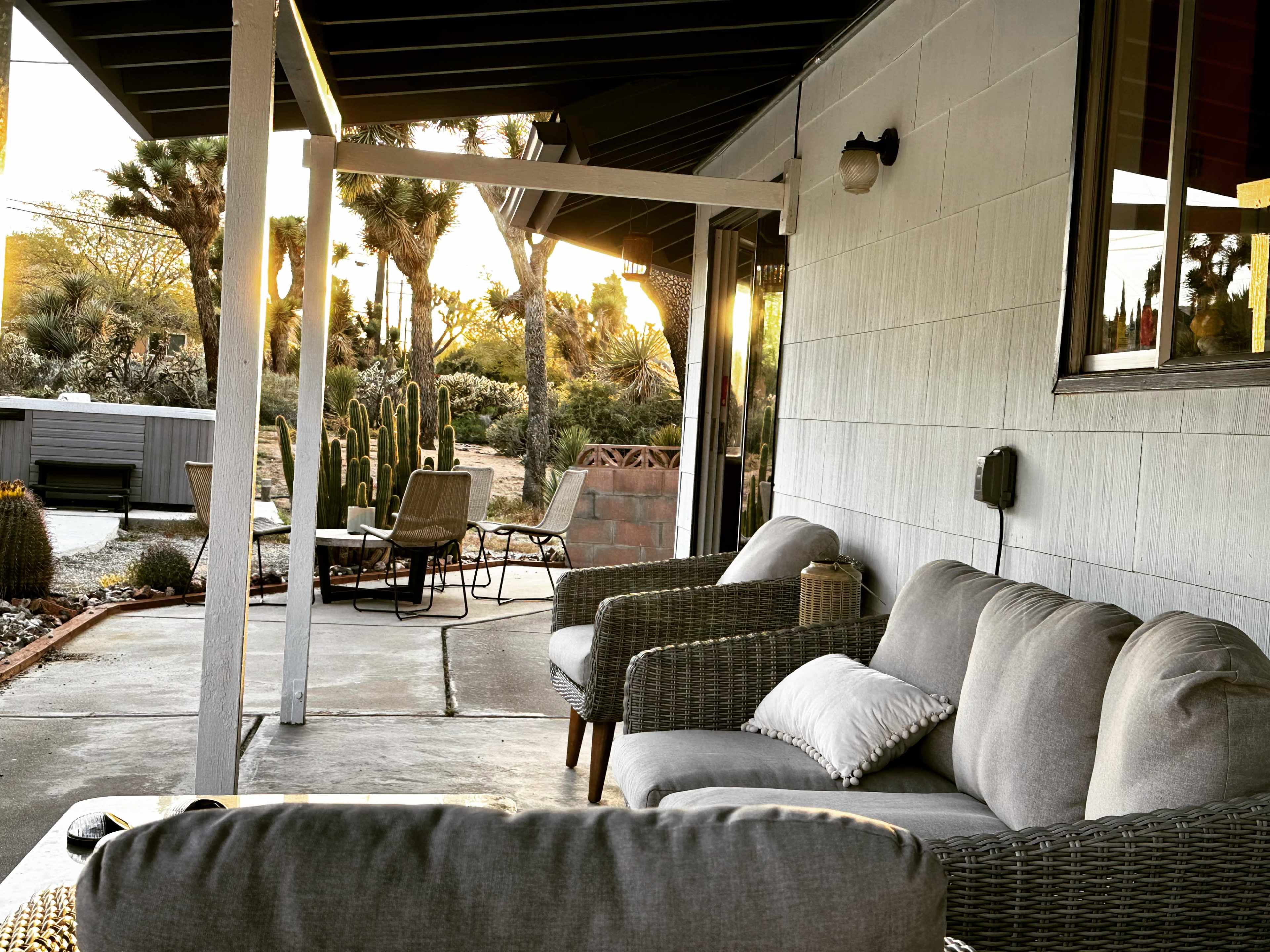A porch with gray sofas and a lantern overlooks a desert landscape with cacti at sunset.