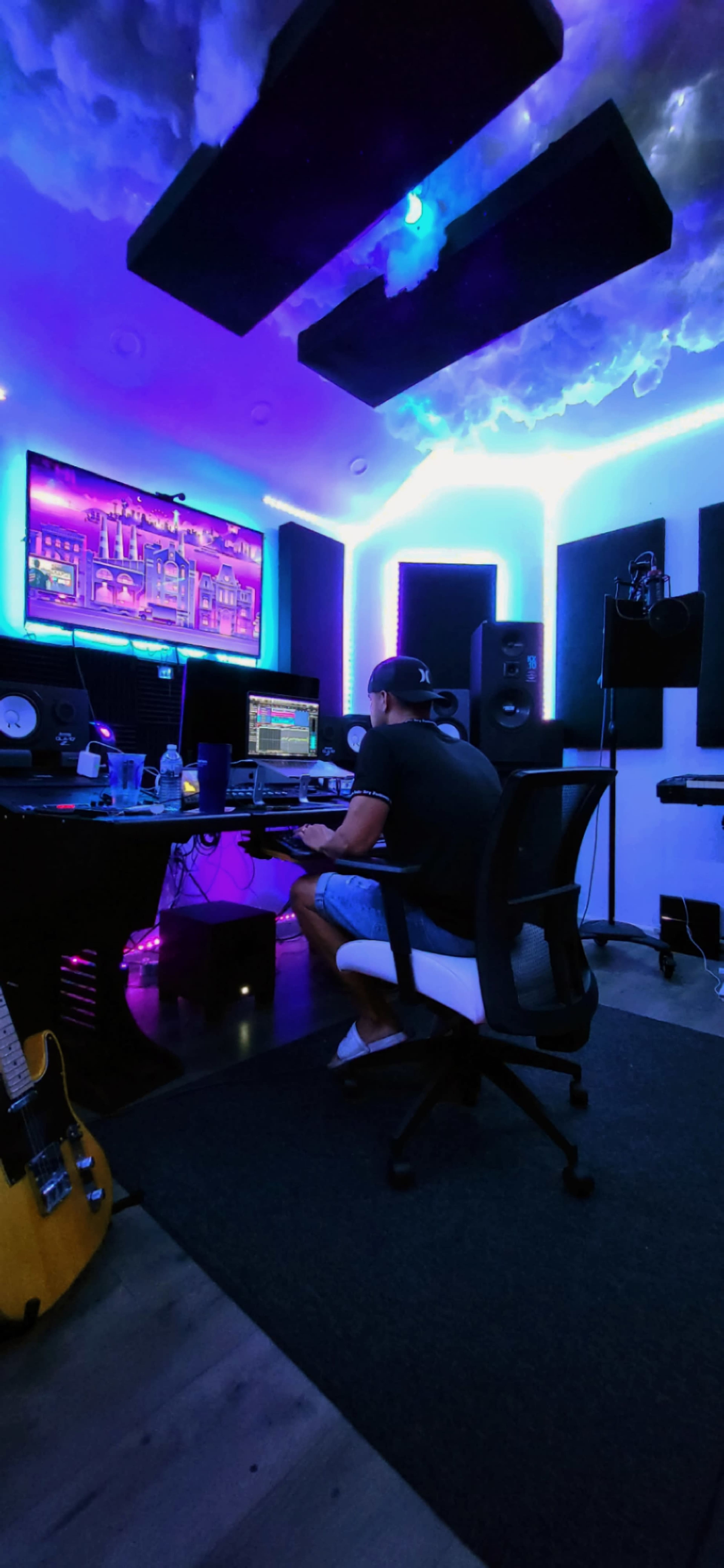 A person sits in a chair at a music production studio, facing a computer screen with colorful lighting illuminating the space.