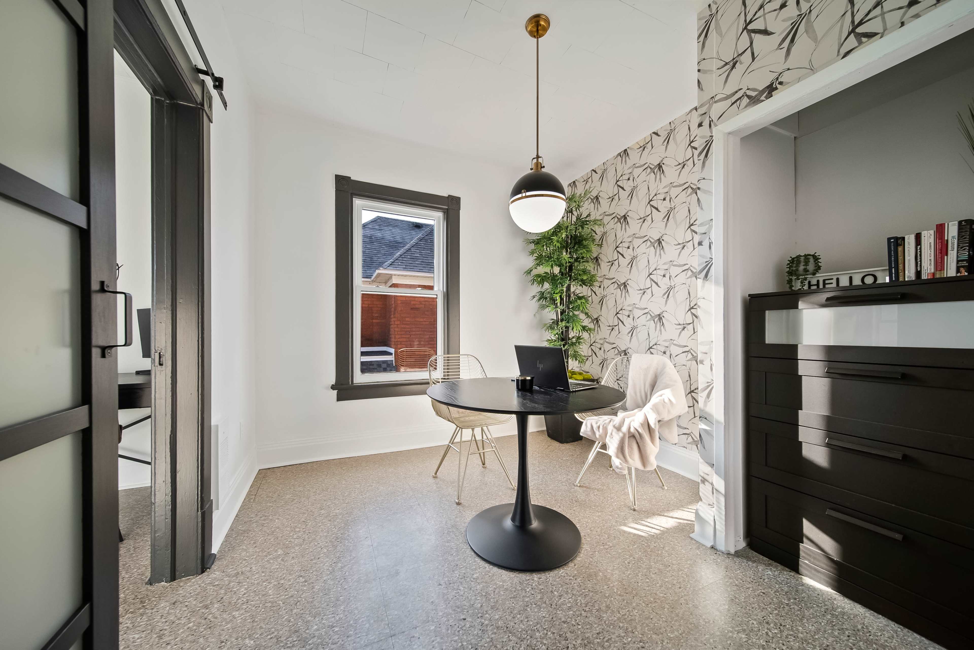 A brightly lit small dining area with a round table, two chairs, and a decorative wall with a plant.
