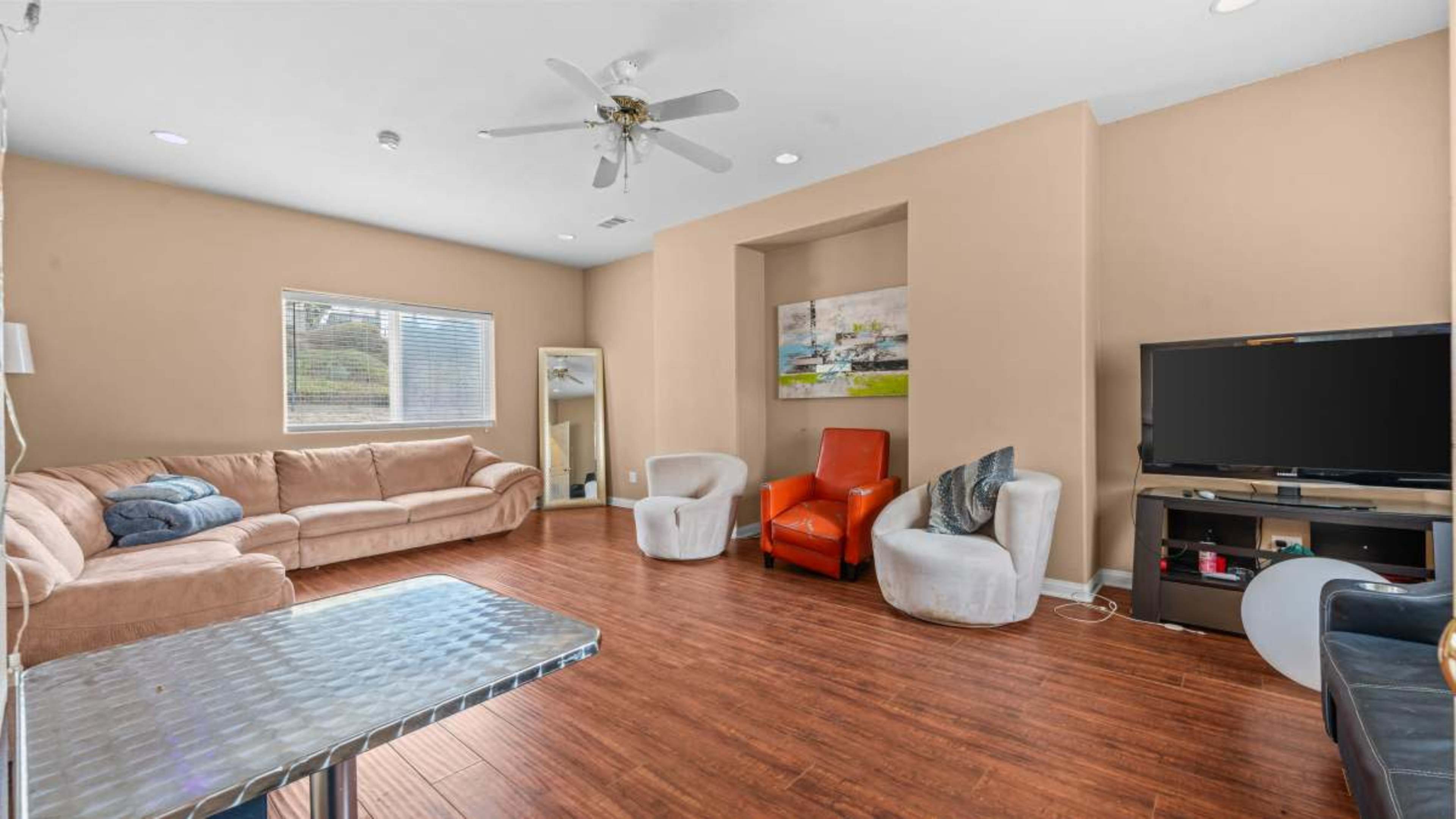 The image shows a living room with a light-colored sofa, a mirror, a couple of armchairs, and a television on a stand.