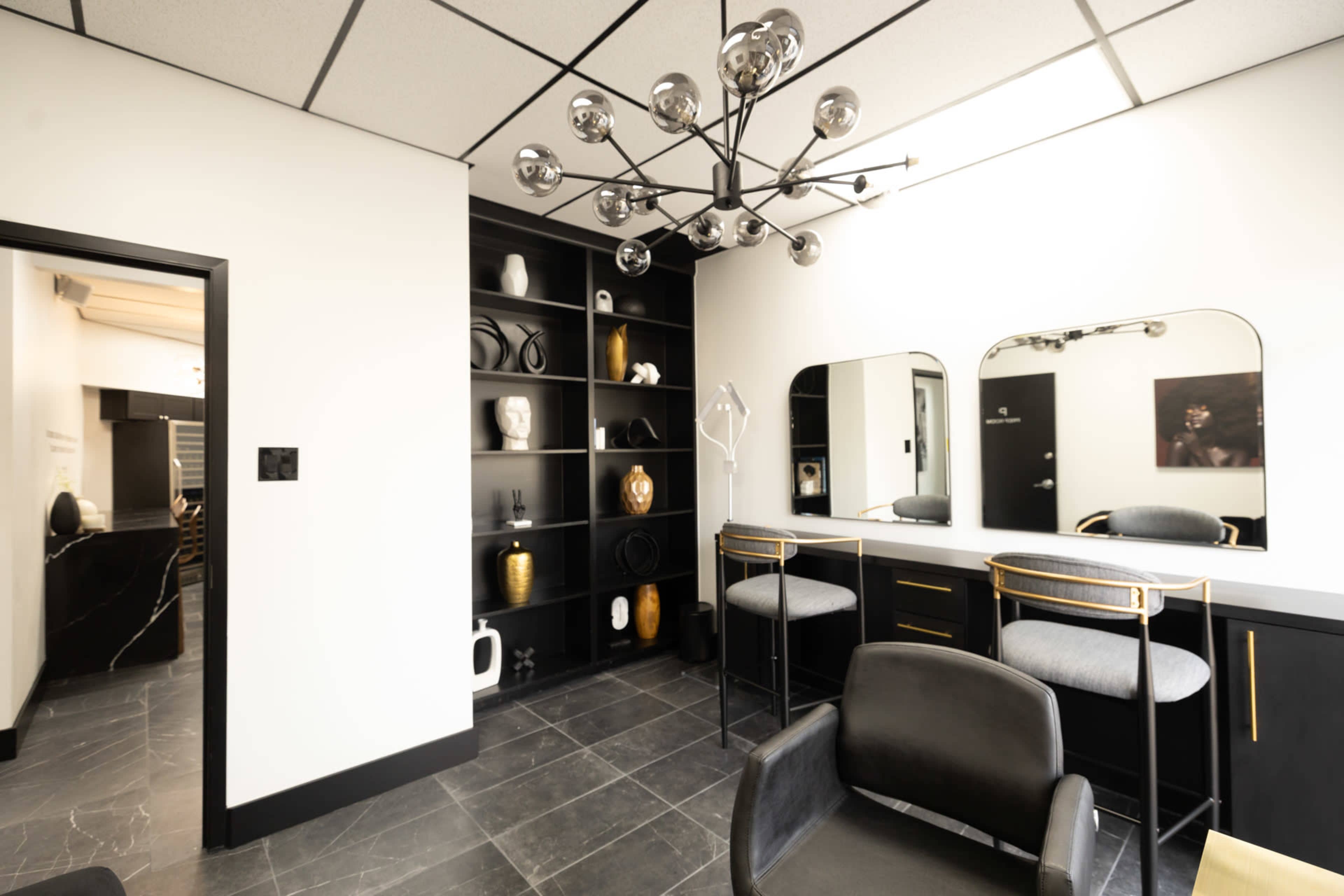 The image shows a modern salon interior featuring a black and white color scheme, a large mirror, stylish lighting fixtures, and organized shelves displaying decorative items.